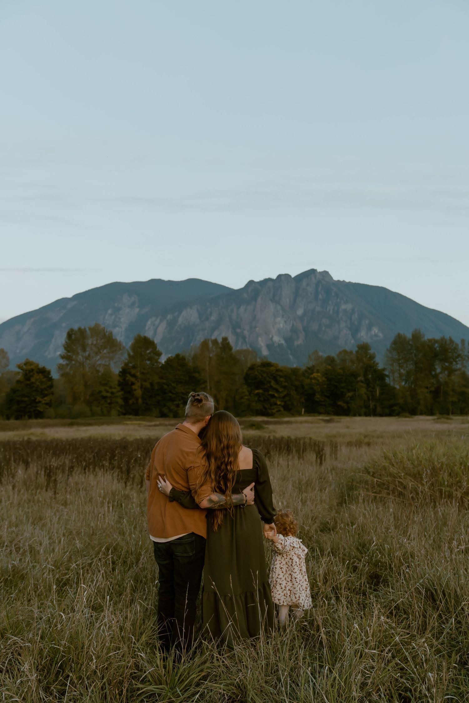 Mountain landscape serves as backdrop for outdoor photoshoot in tall grass meadow at golden hour.
