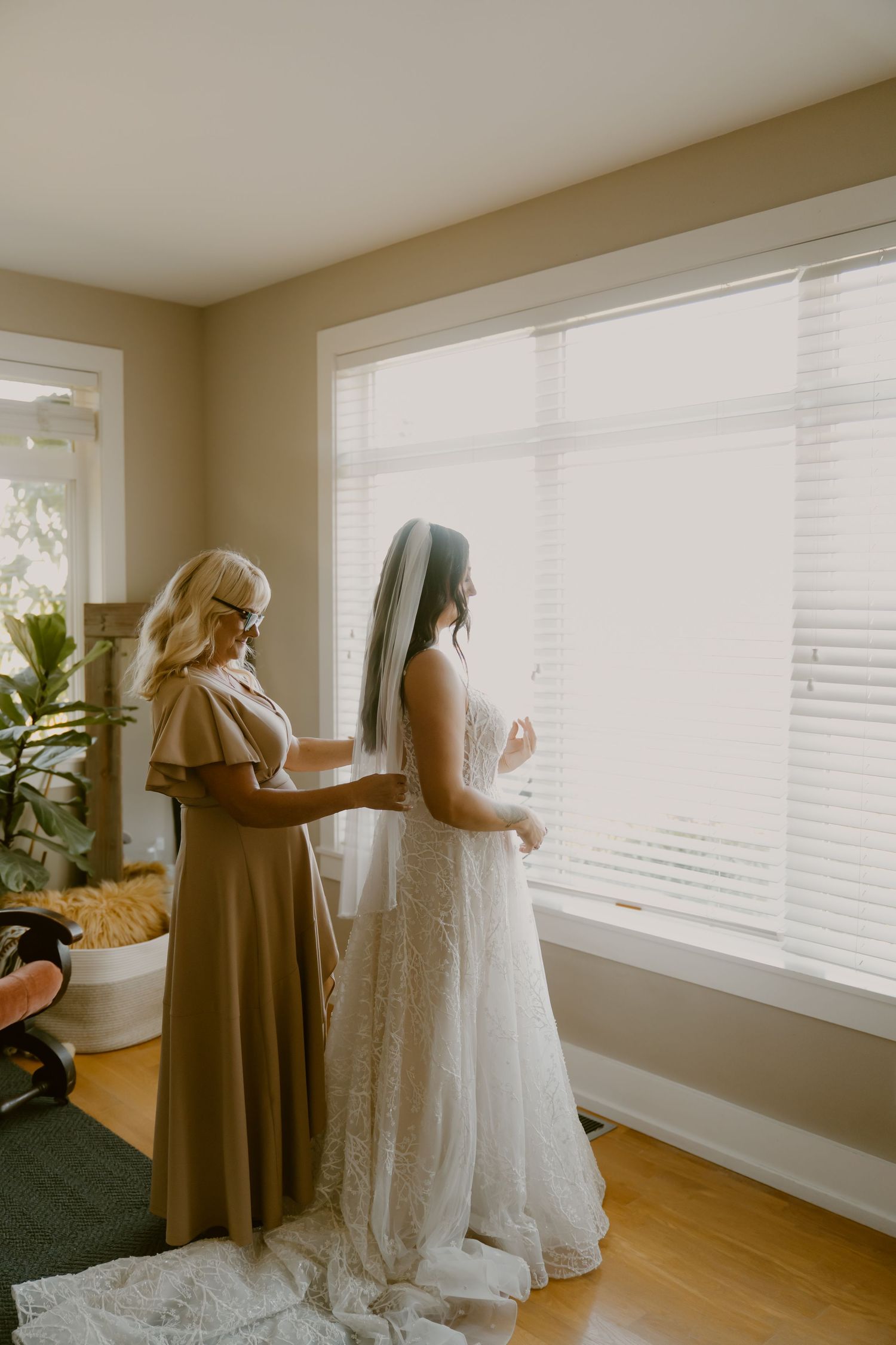 A wedding dress fitting session in a bright, sunlit room with wooden floors.