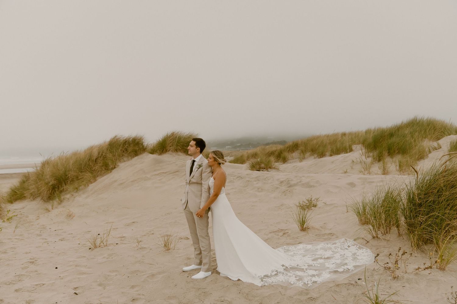 Bride and groom share intimate moment on sandy beach dunes.