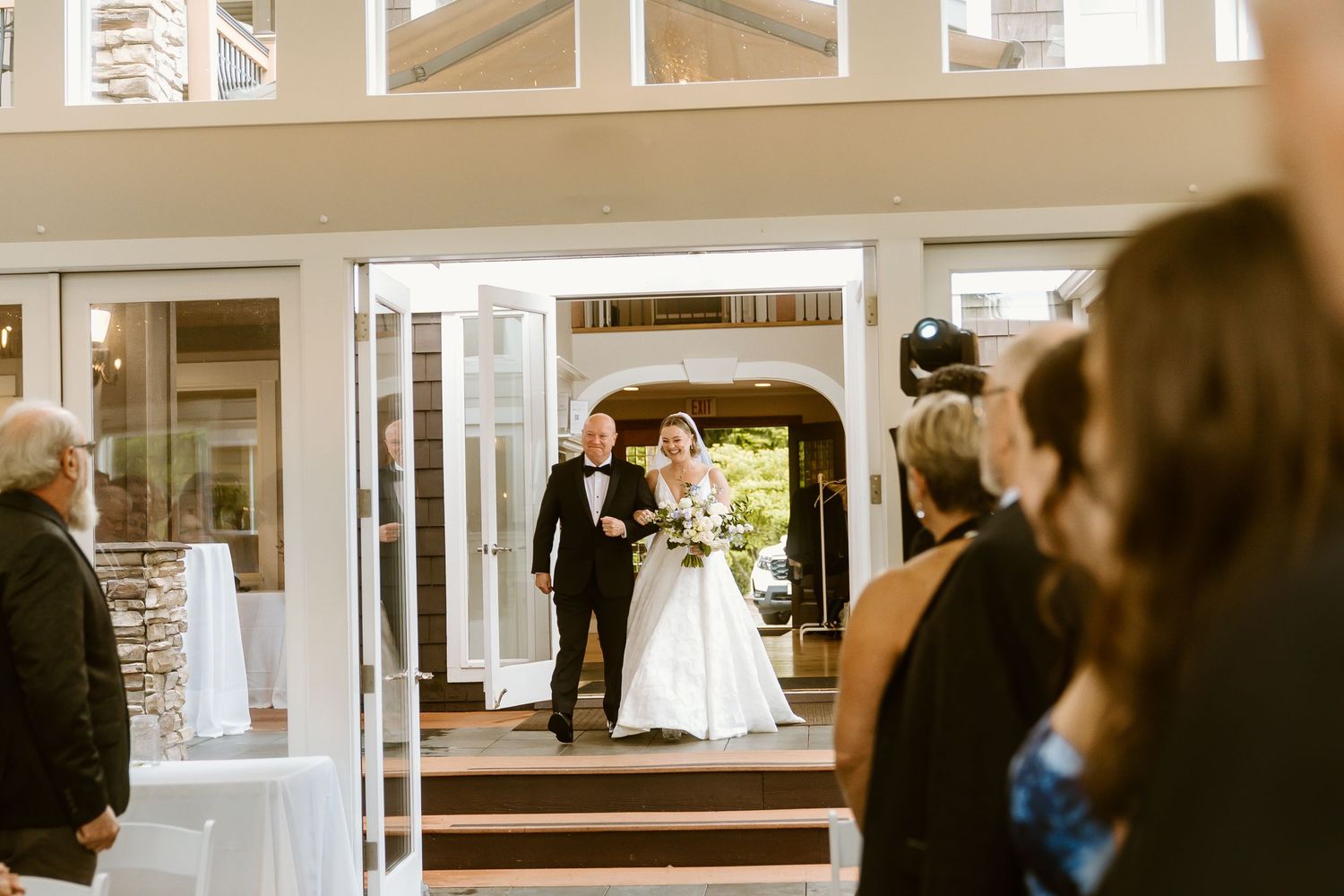 Bride and groom entering wedding reception through elegant glass doors while guests watch the grand entrance.