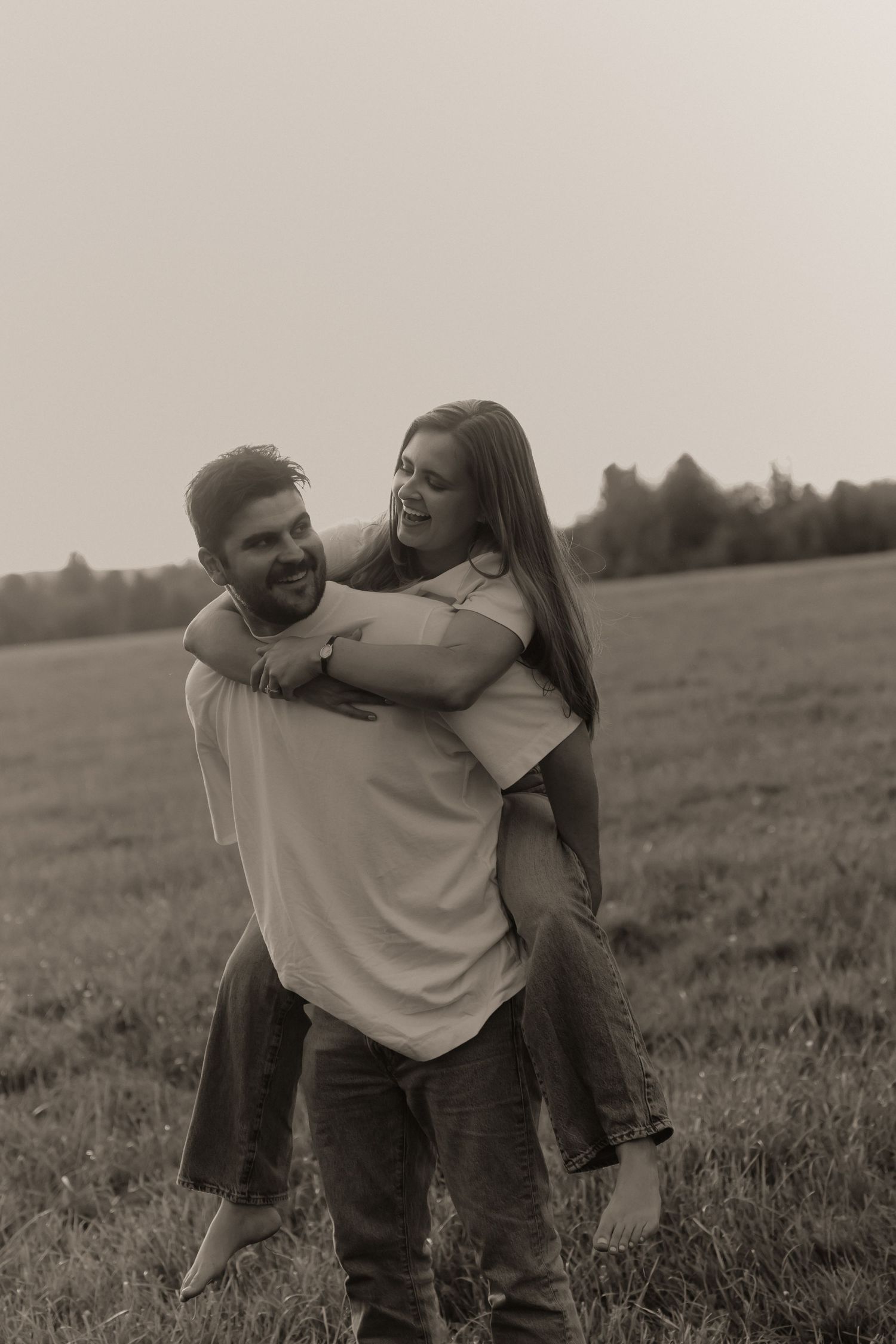 Black and white photo of a happy couple, man giving woman a piggyback ride in an open field.