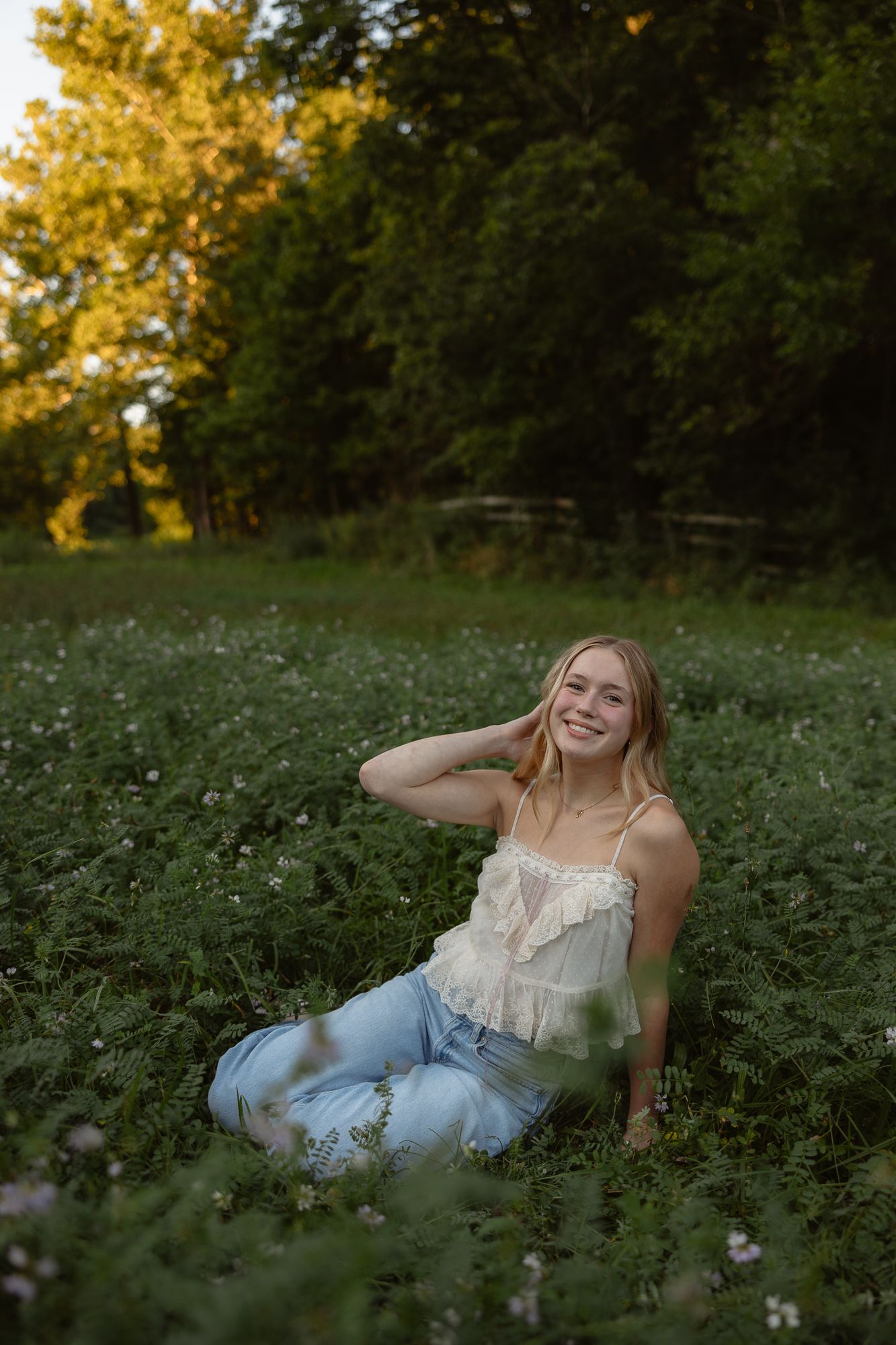 A person sits in a wildflower meadow at golden hour wearing a white lace top and jeans among blooming flowers.