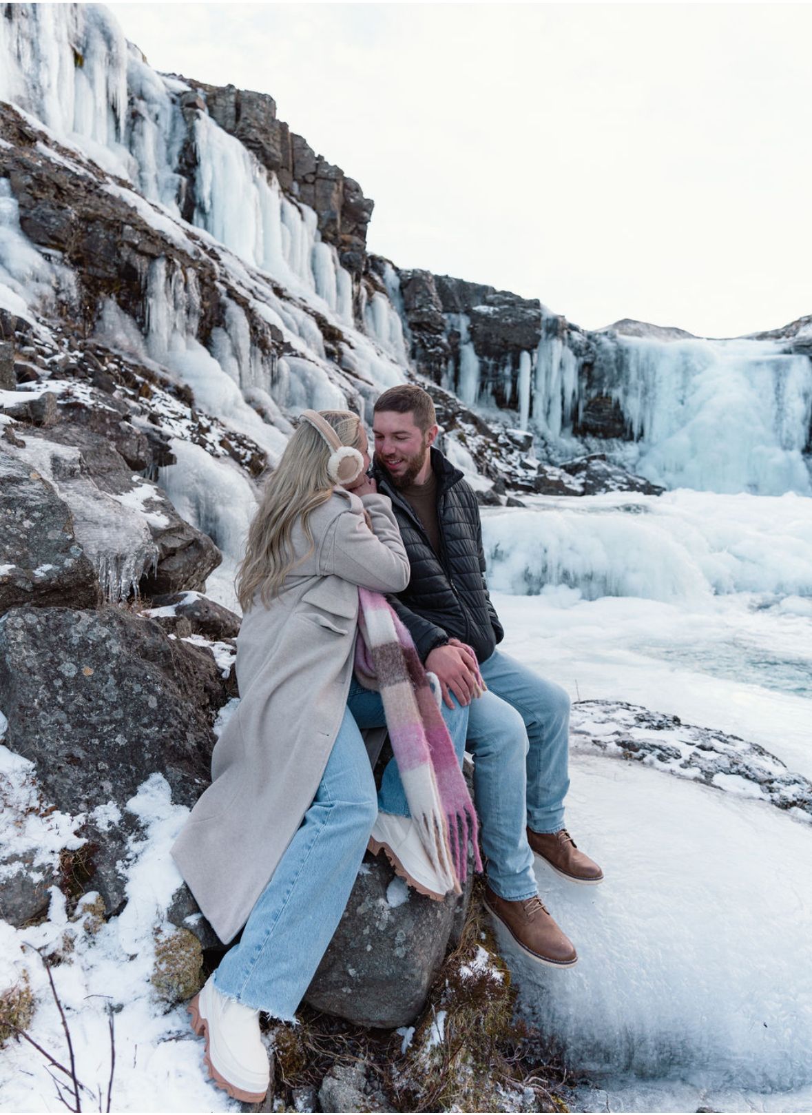 Couple sitting on a big rock on a icey waterfall Iceland