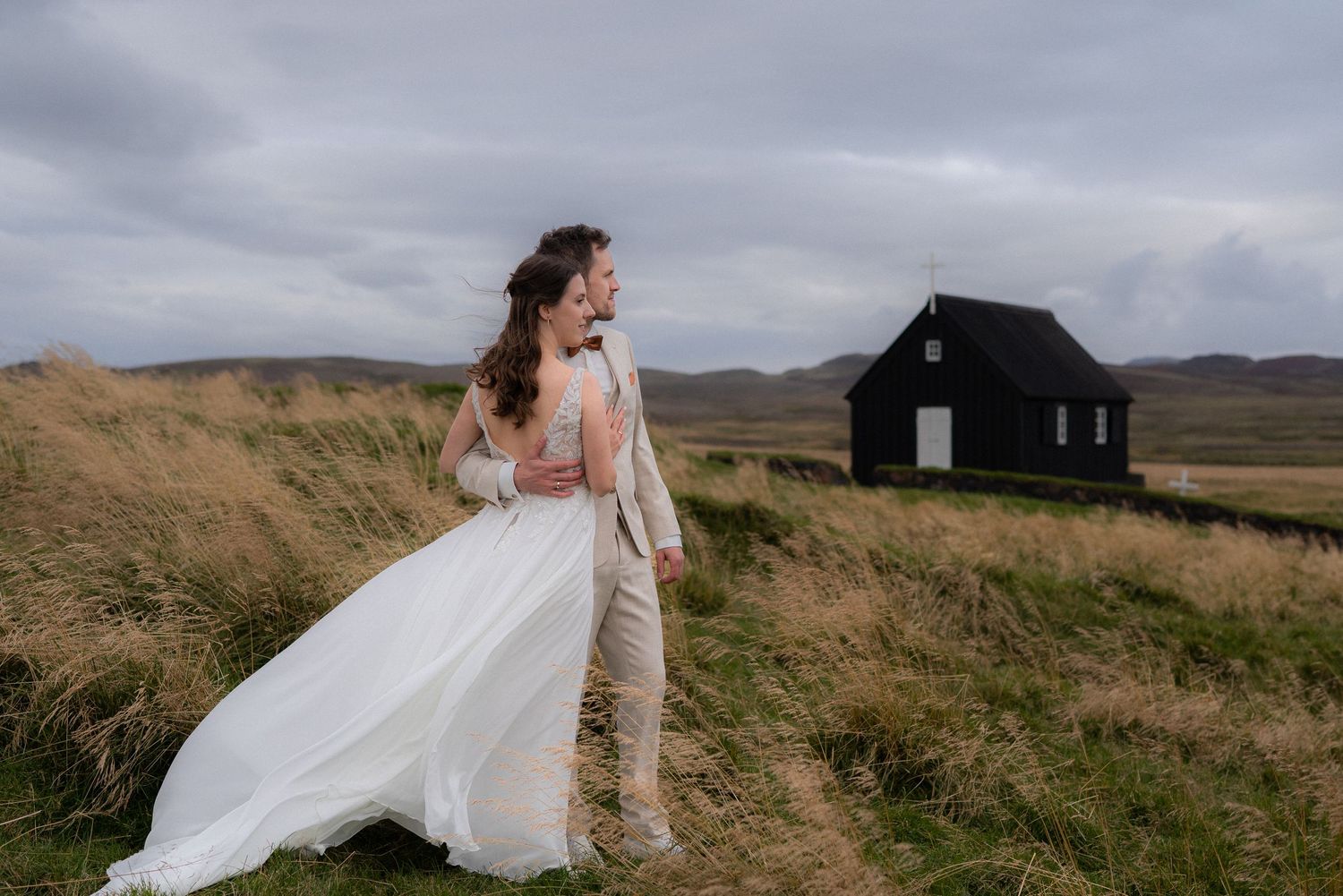 Elopement couple embracing near Krýsuvíkurkirkja church in Iceland looking into the distance