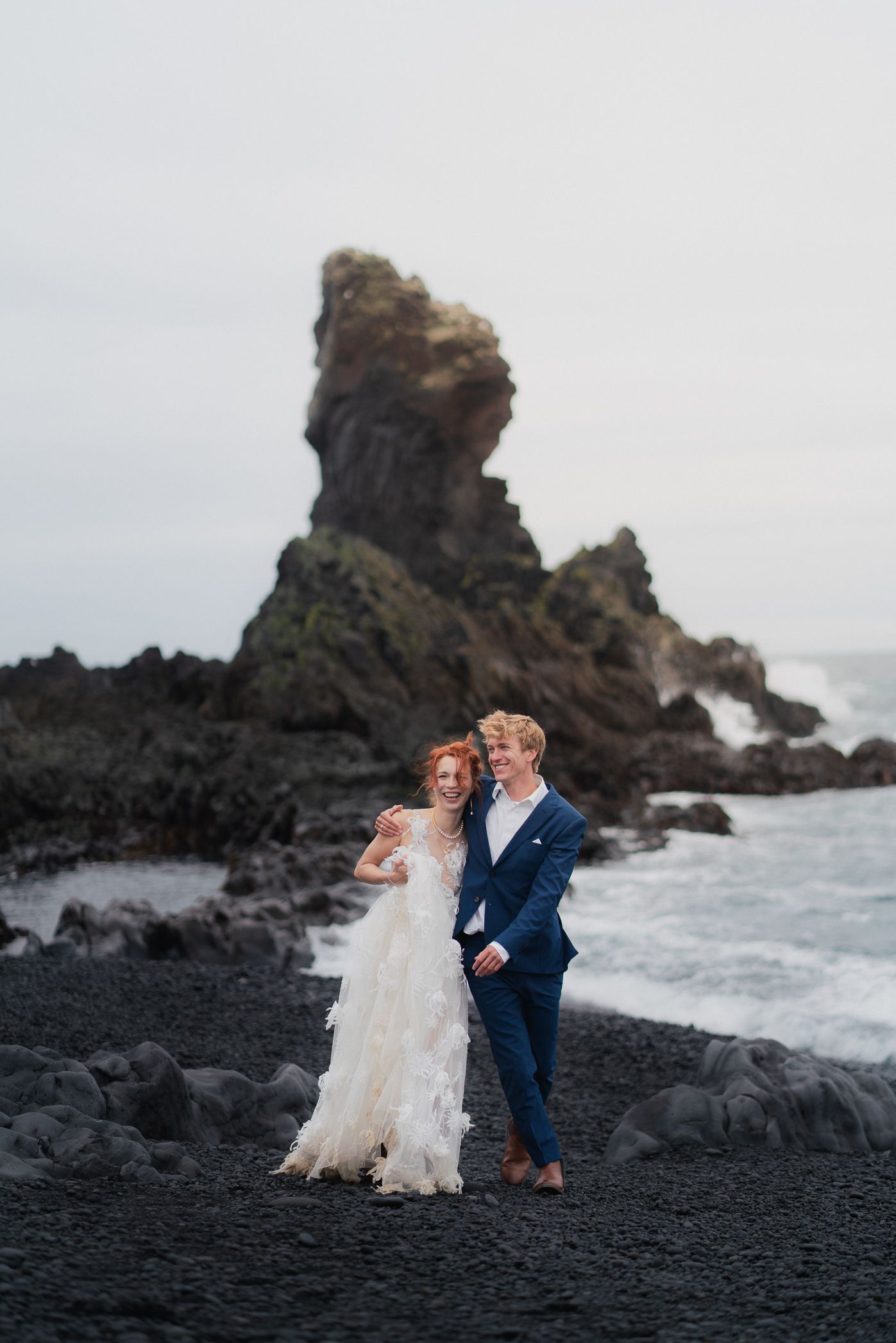 Couple walking happily on a black sand beach.