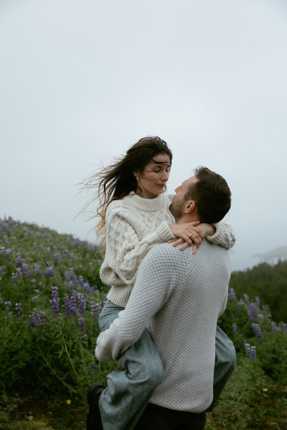 Couple in a lupine field at Þingvallavatn as he lifts her up in Iceland’s summer landscape