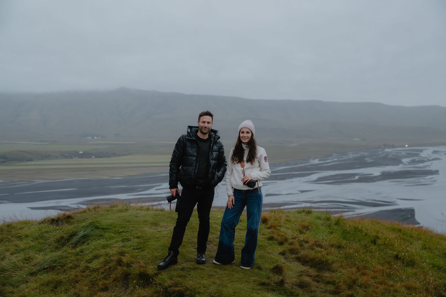 Professional elopement photographer couple in Iceland standing on a hilltop overlooking the coast