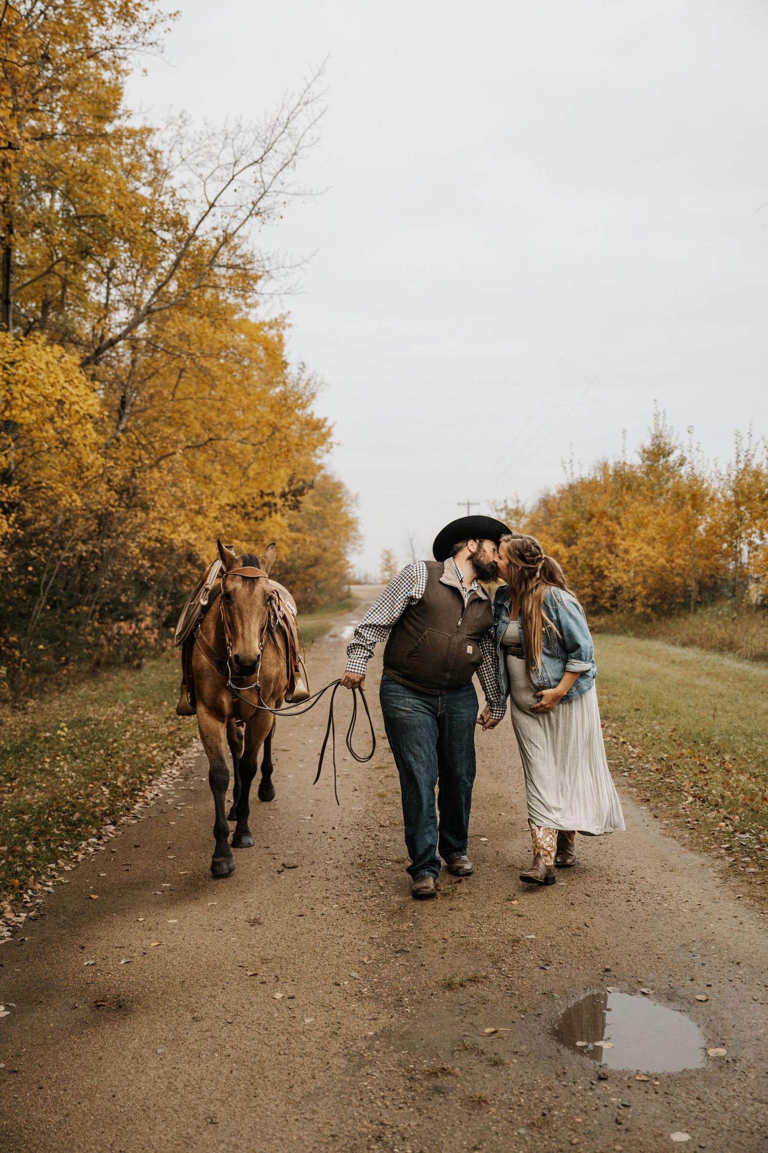 A romantic autumn walk along a dirt path with a horse following behind in golden fall foliage.