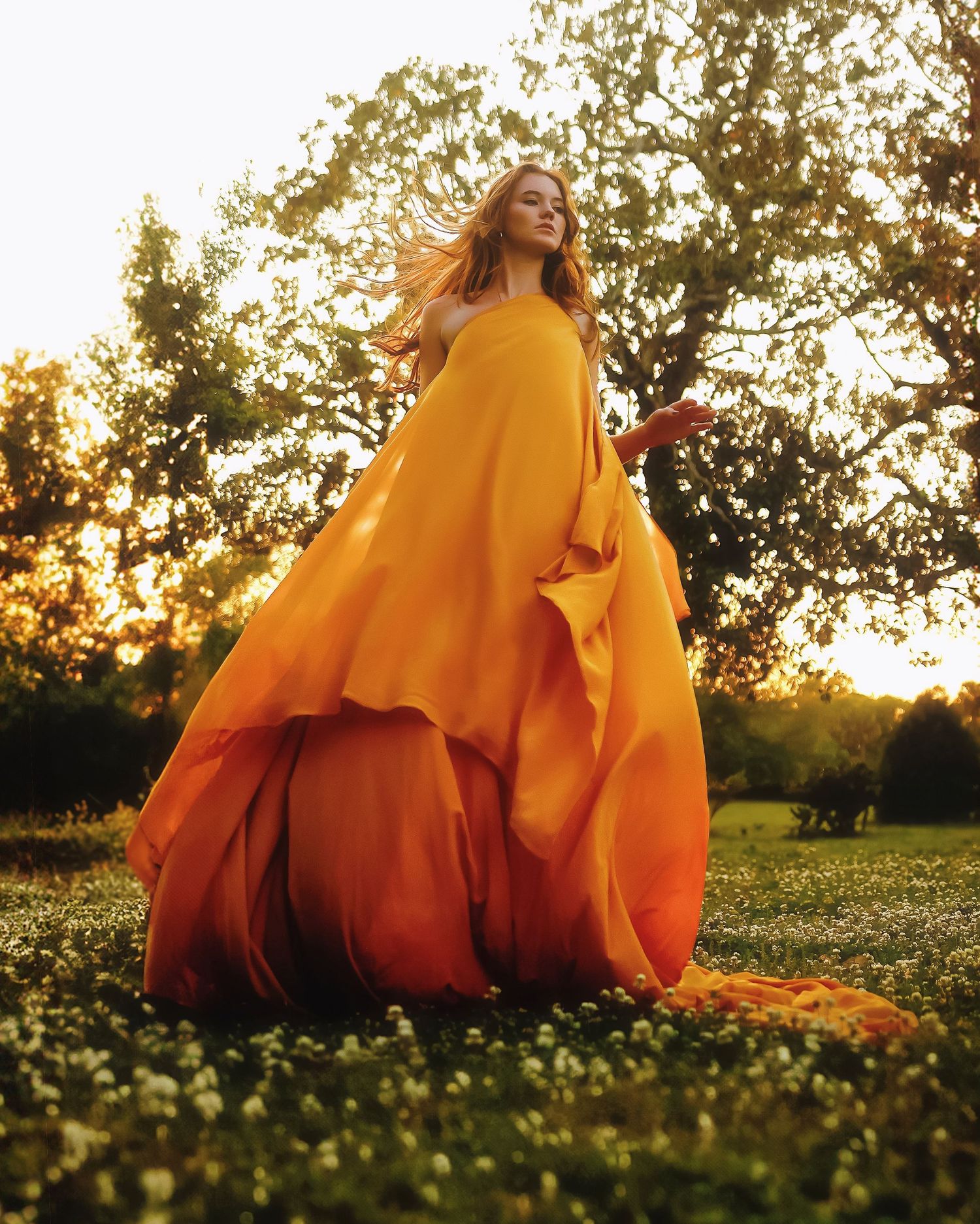 Person in flowing orange gown twirls gracefully in a wildflower meadow during golden sunset light.