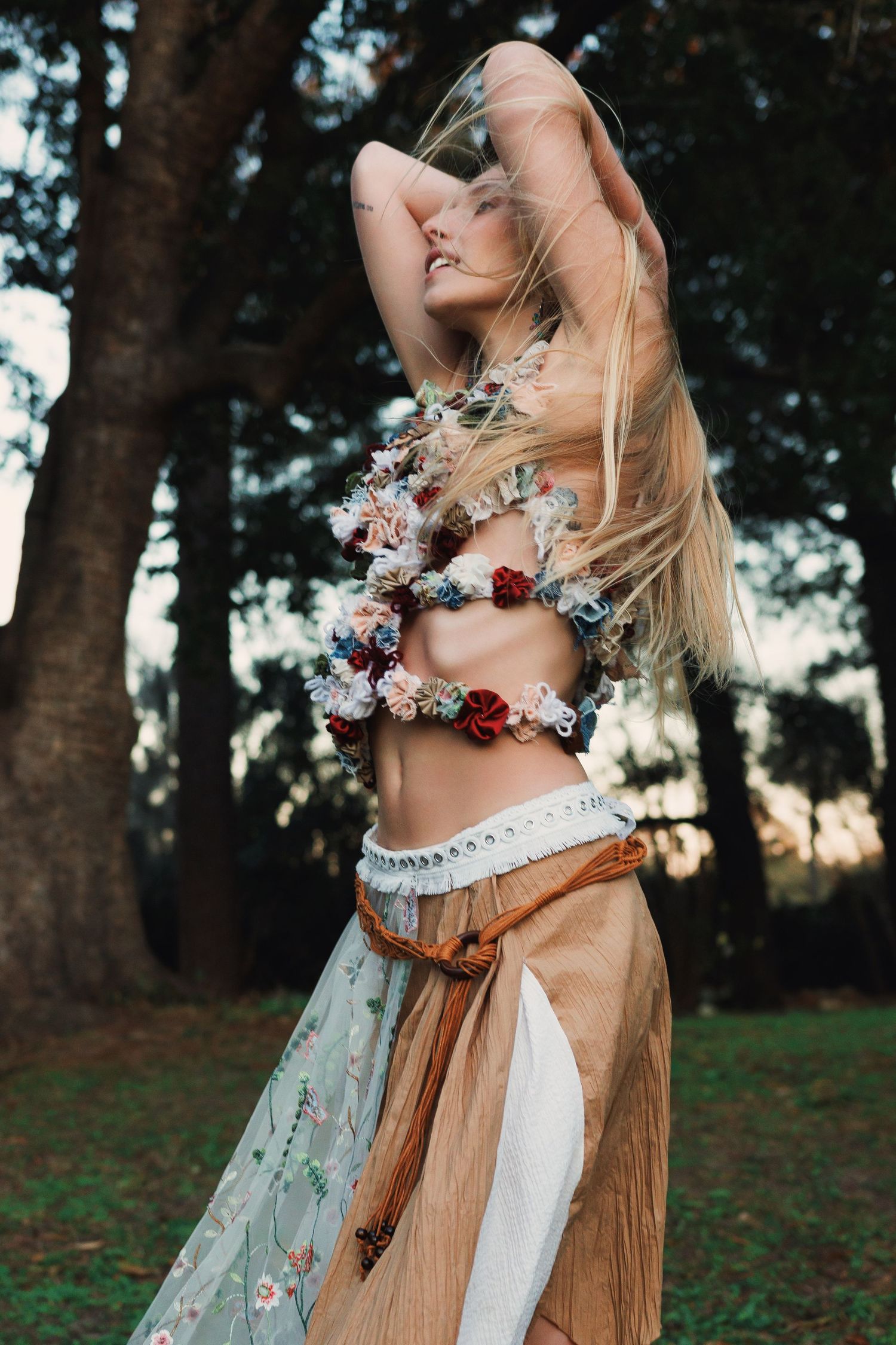 A person wearing a floral crown and medieval-style dress twirls in a forest setting at golden hour.