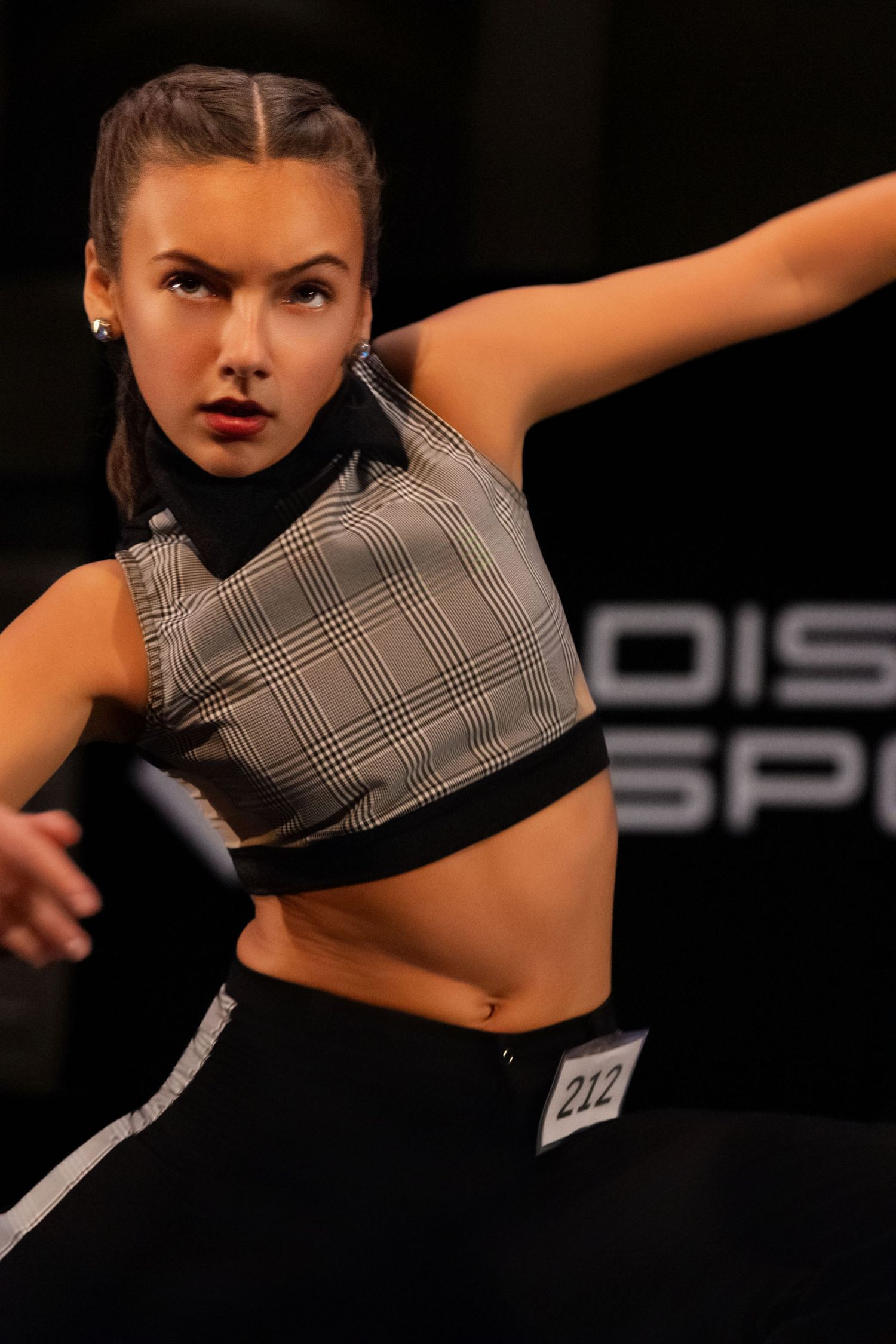 Dancer performs dynamic movements in black and white checkered crop top against dark background during performance.