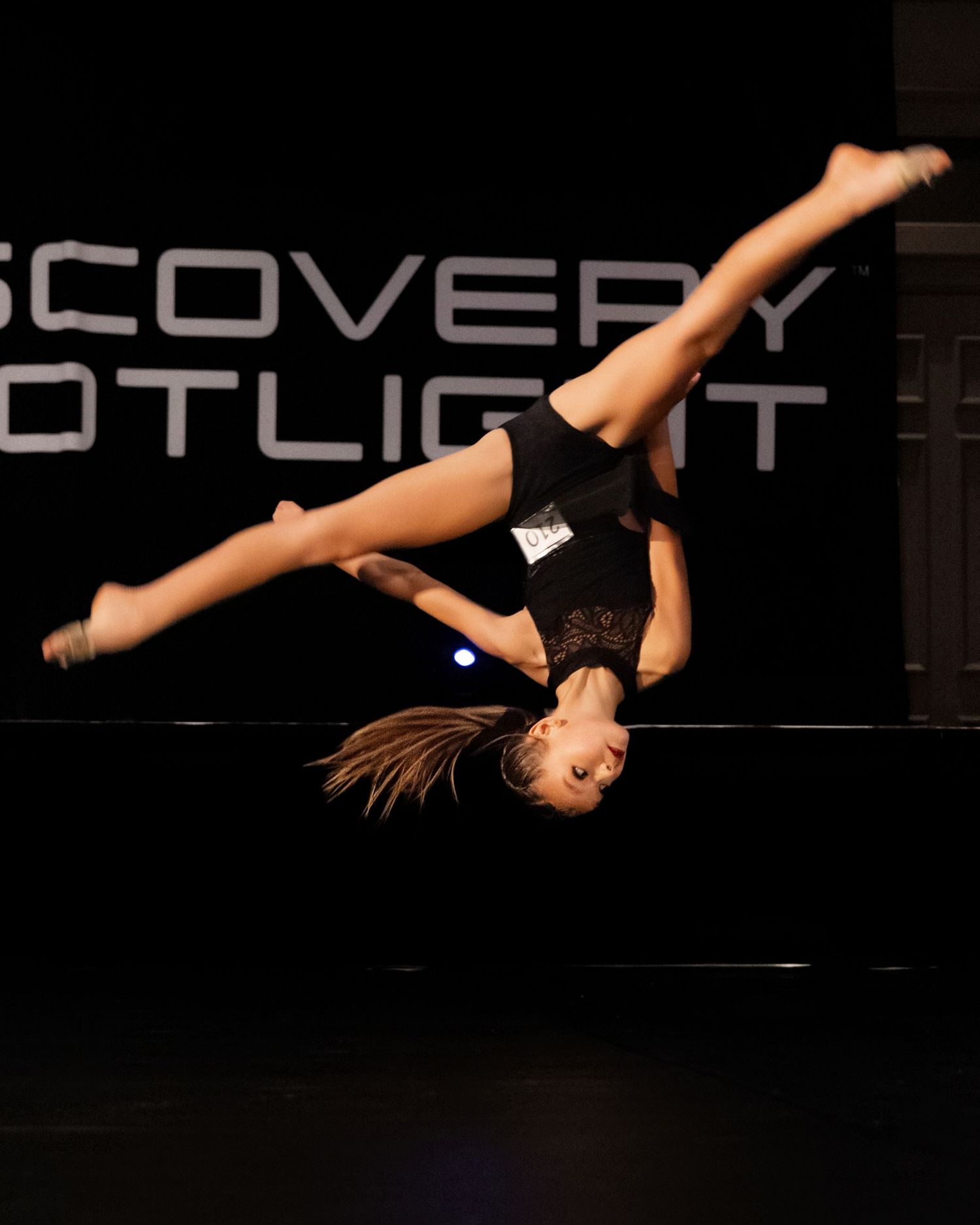 Gymnast performing a graceful aerial backflip sequence in a dark studio with dramatic lighting.