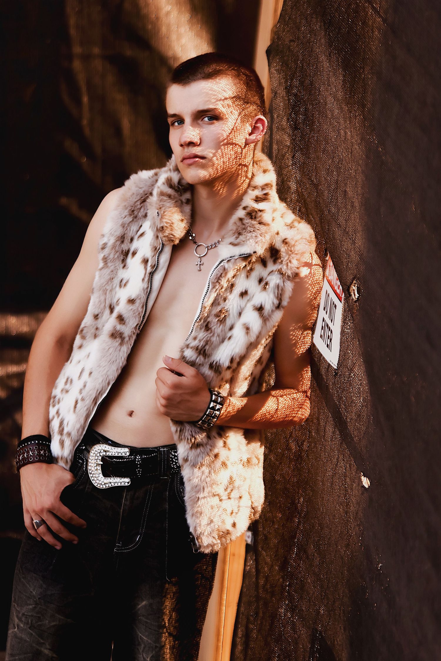 Person wearing leopard print fur vest and dark jeans poses against textured wall in dramatic lighting.