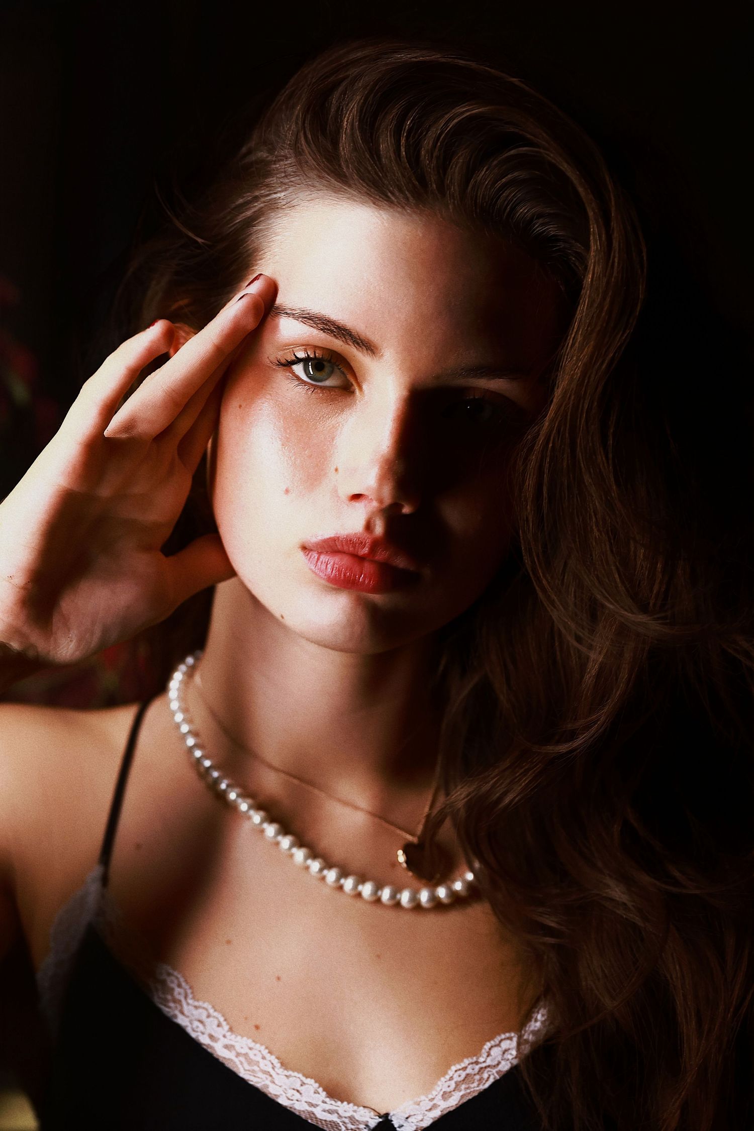 Classic glamour portrait with dramatic lighting features elegant pearl necklace and lace detail against dark background.