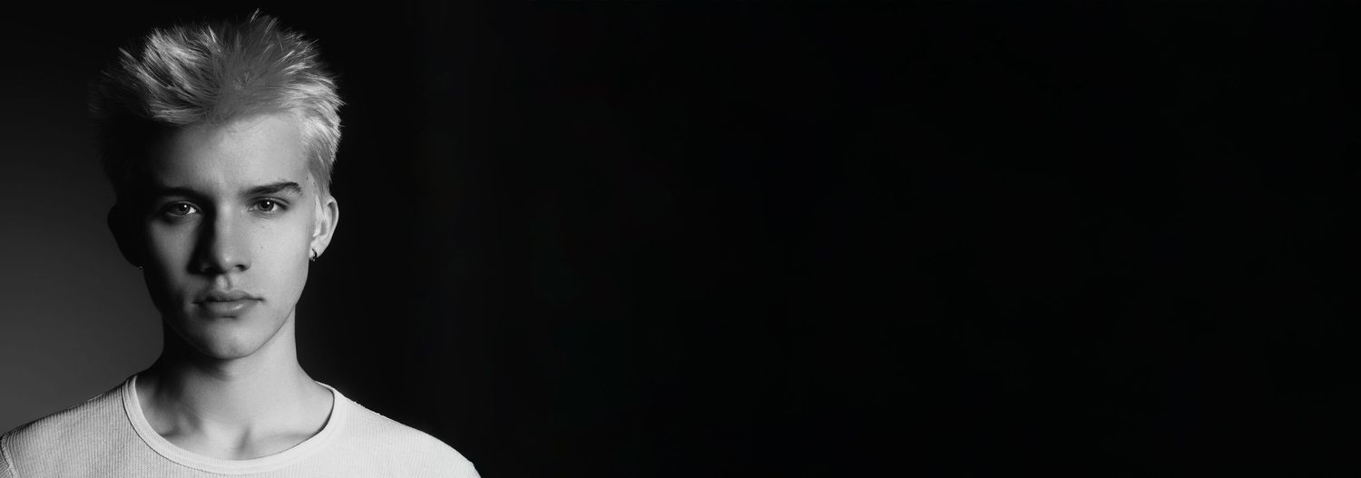 Black and white portrait photo of a young person in a white t-shirt against a dark background.