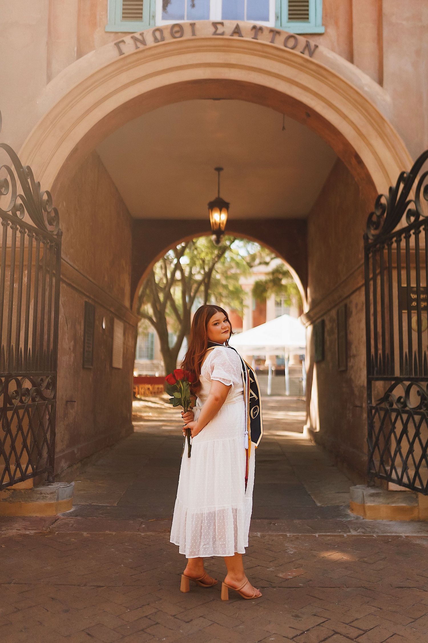 A person in a white dress poses in a series of archways with brick walls and wrought iron gates.