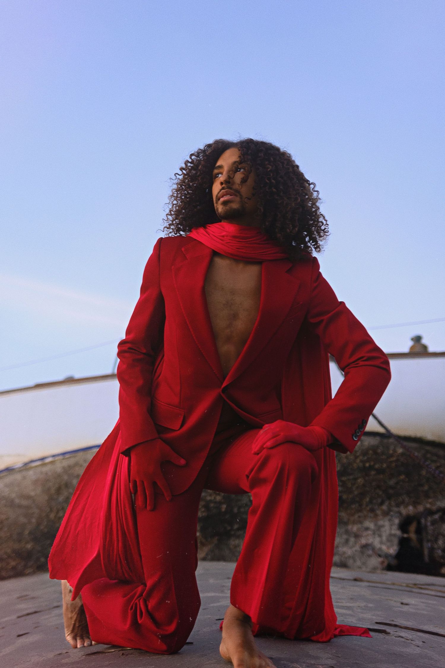 A person in a flowing red dress poses dramatically against a rustic desert landscape at sunset.