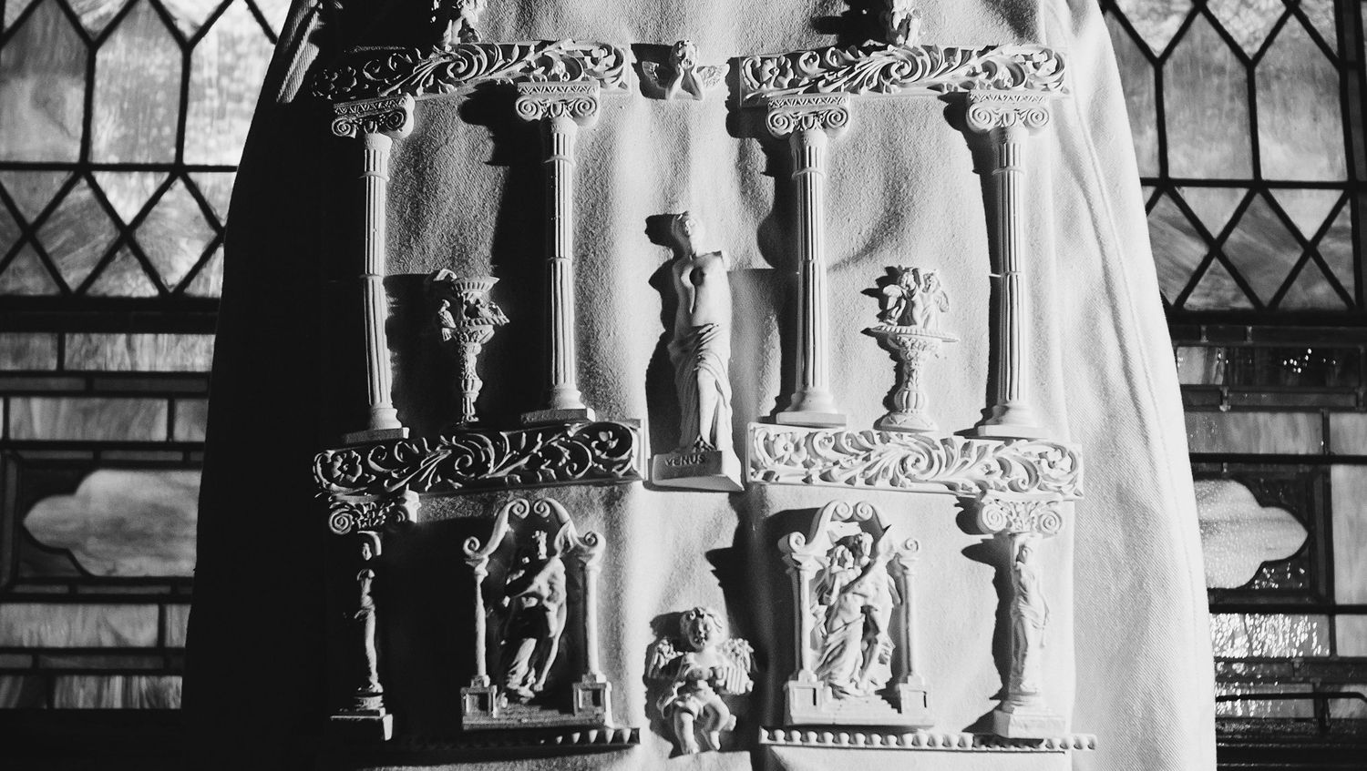 A black and white photo shows a bride and groom holding hands in front of a stained glass church window.