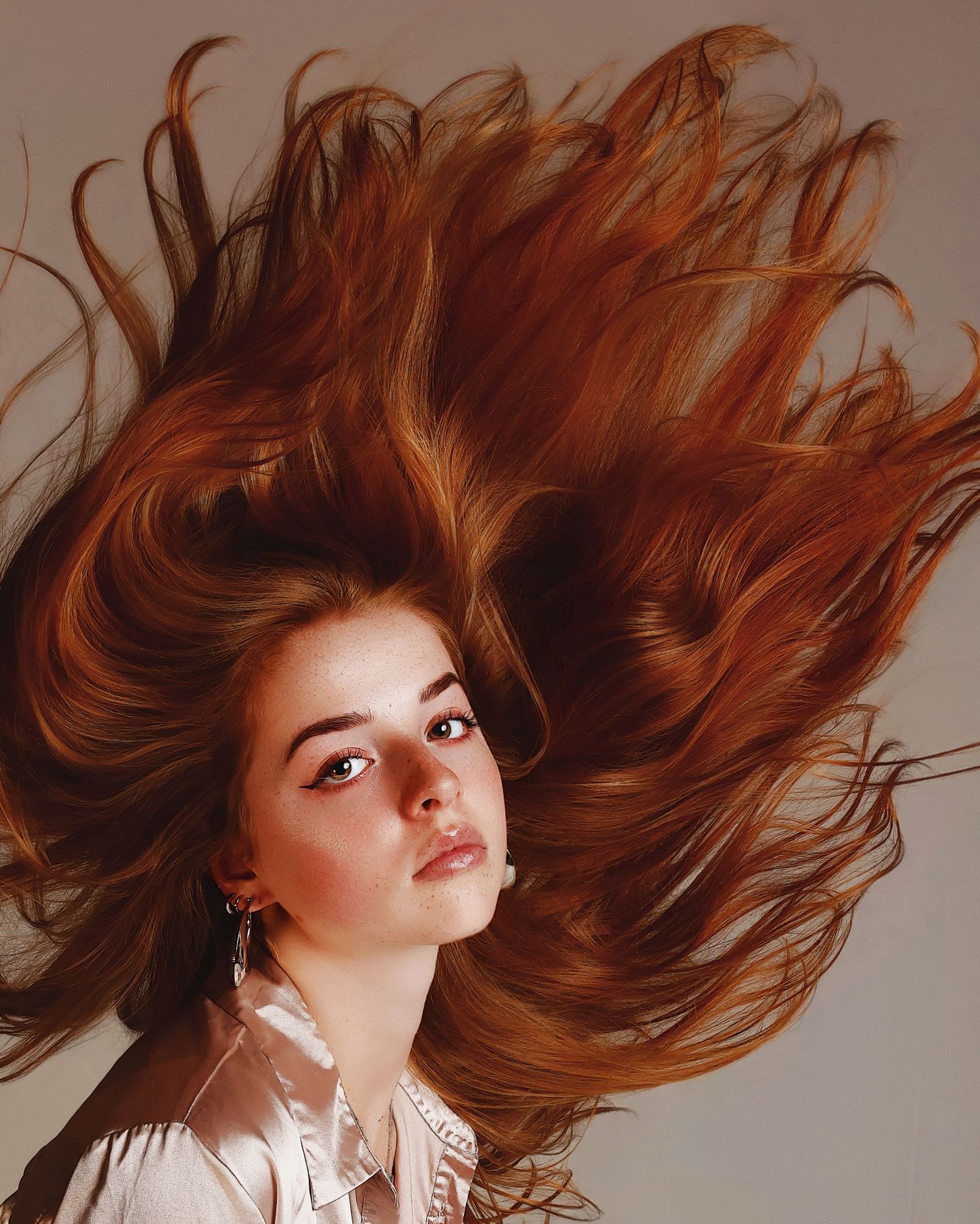 Beautiful windswept red hair spreads dramatically in motion against warm brown backdrop with white blouse.