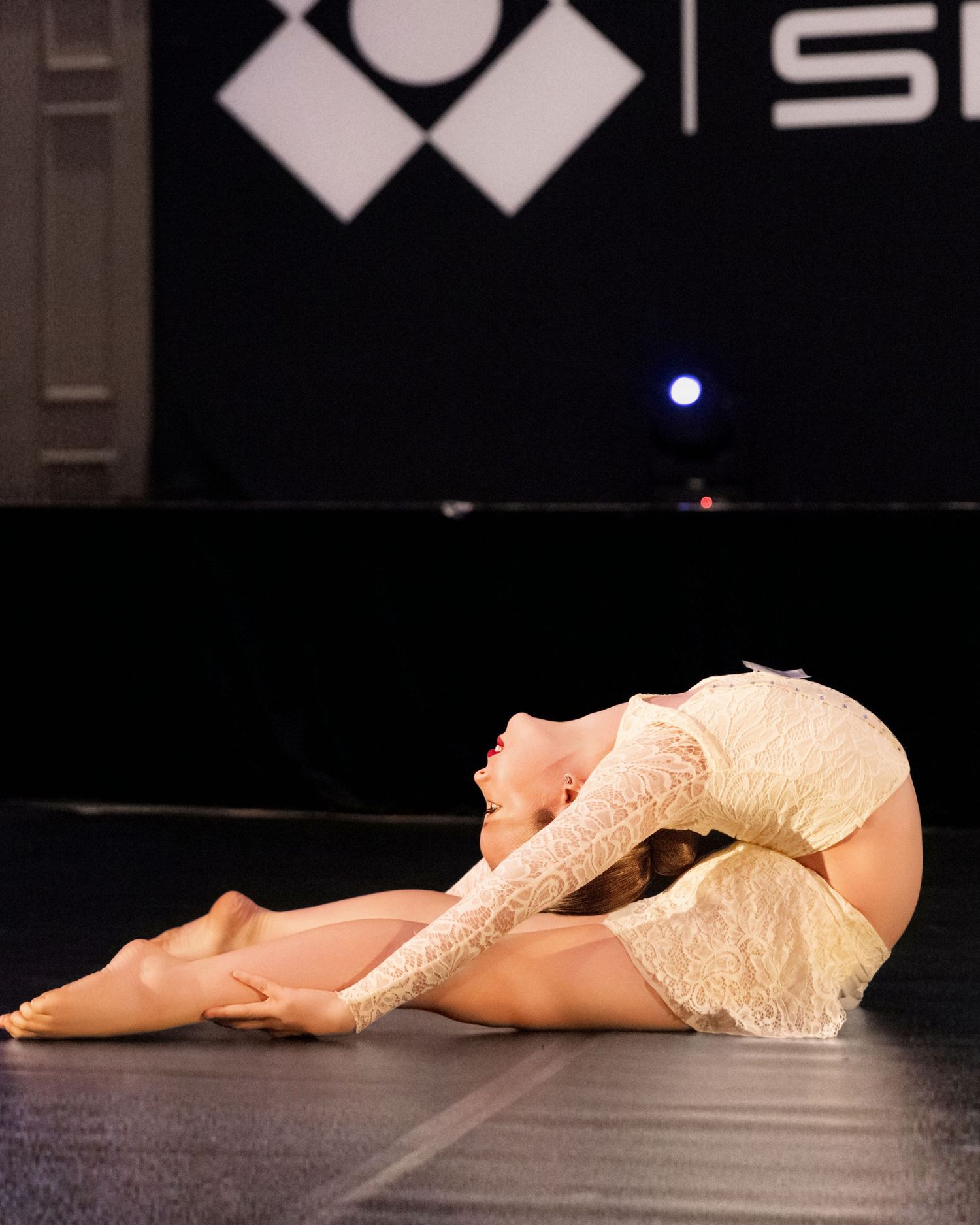 A dancer in a white dress lies gracefully on a dark stage floor in a series of connected performance photos.