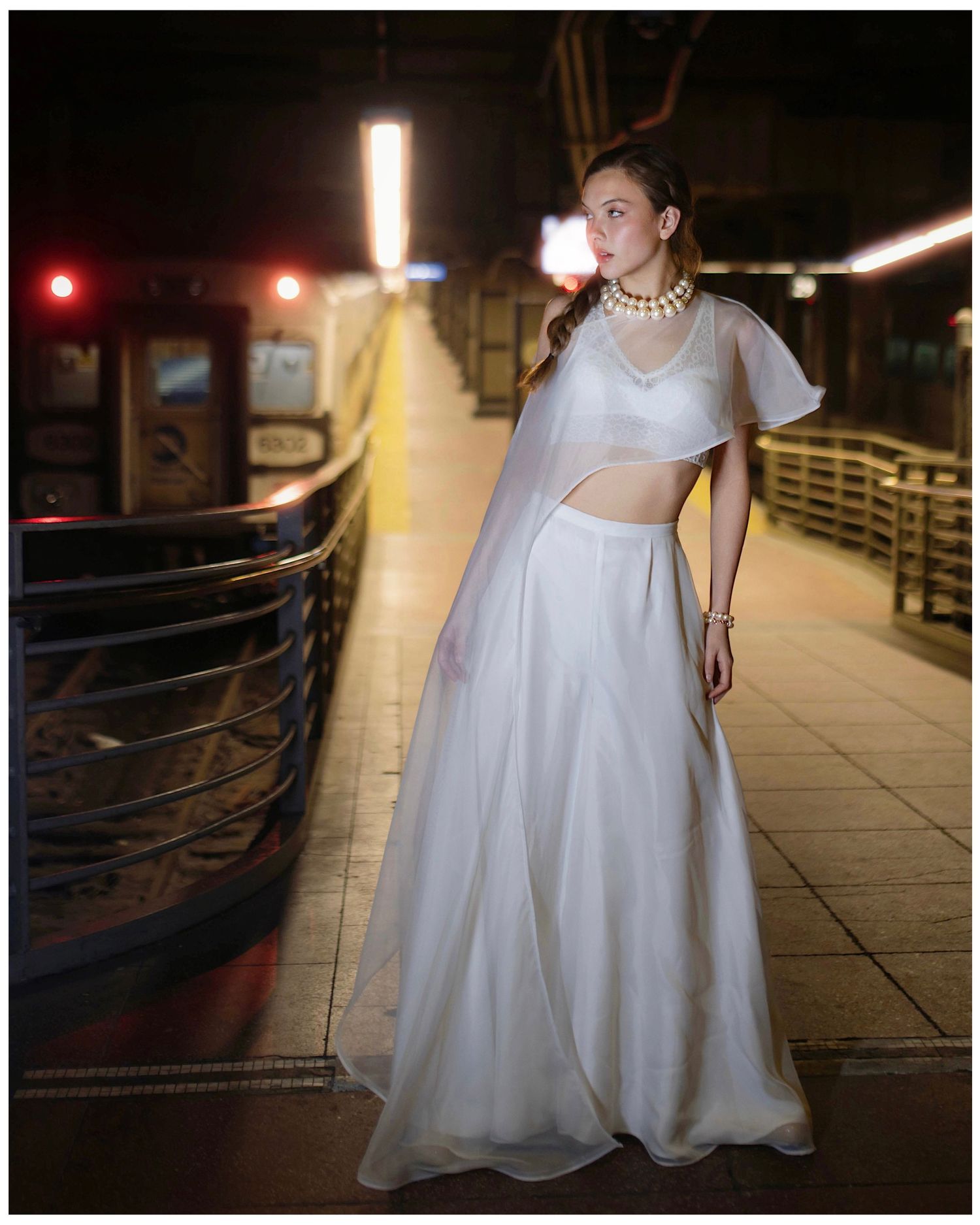 A series of nighttime photos showing someone in a flowing white bridal gown posing against dark railings with city lights.