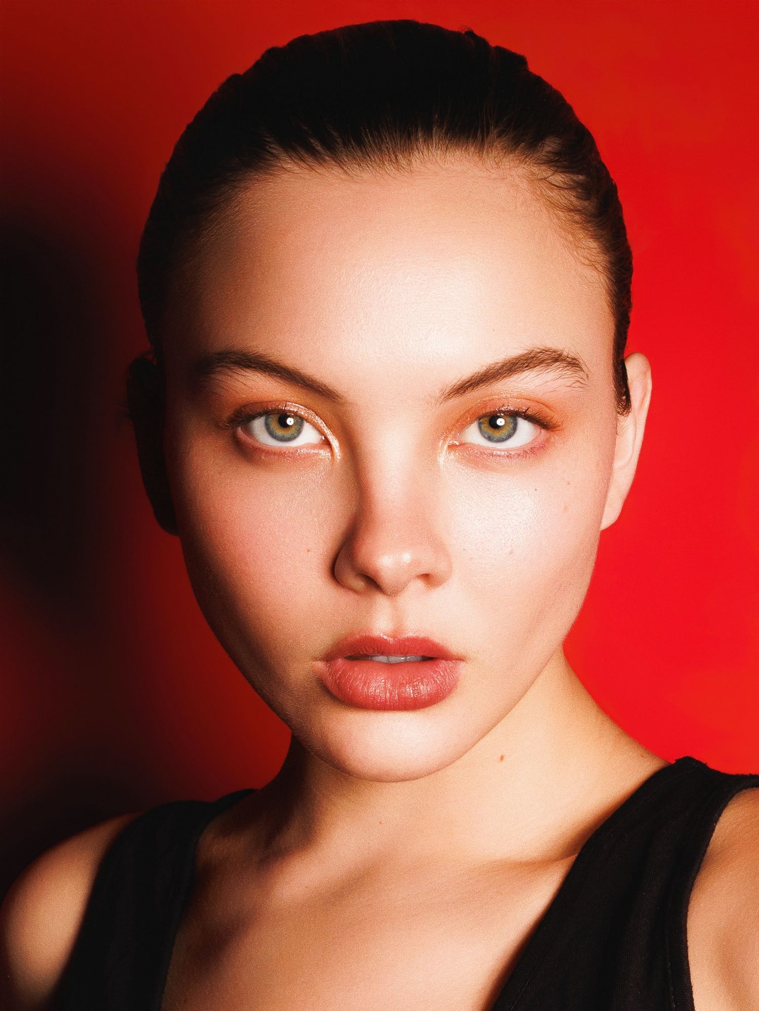Beauty portrait with striking eyes and bold red lips against dramatic crimson background lighting.