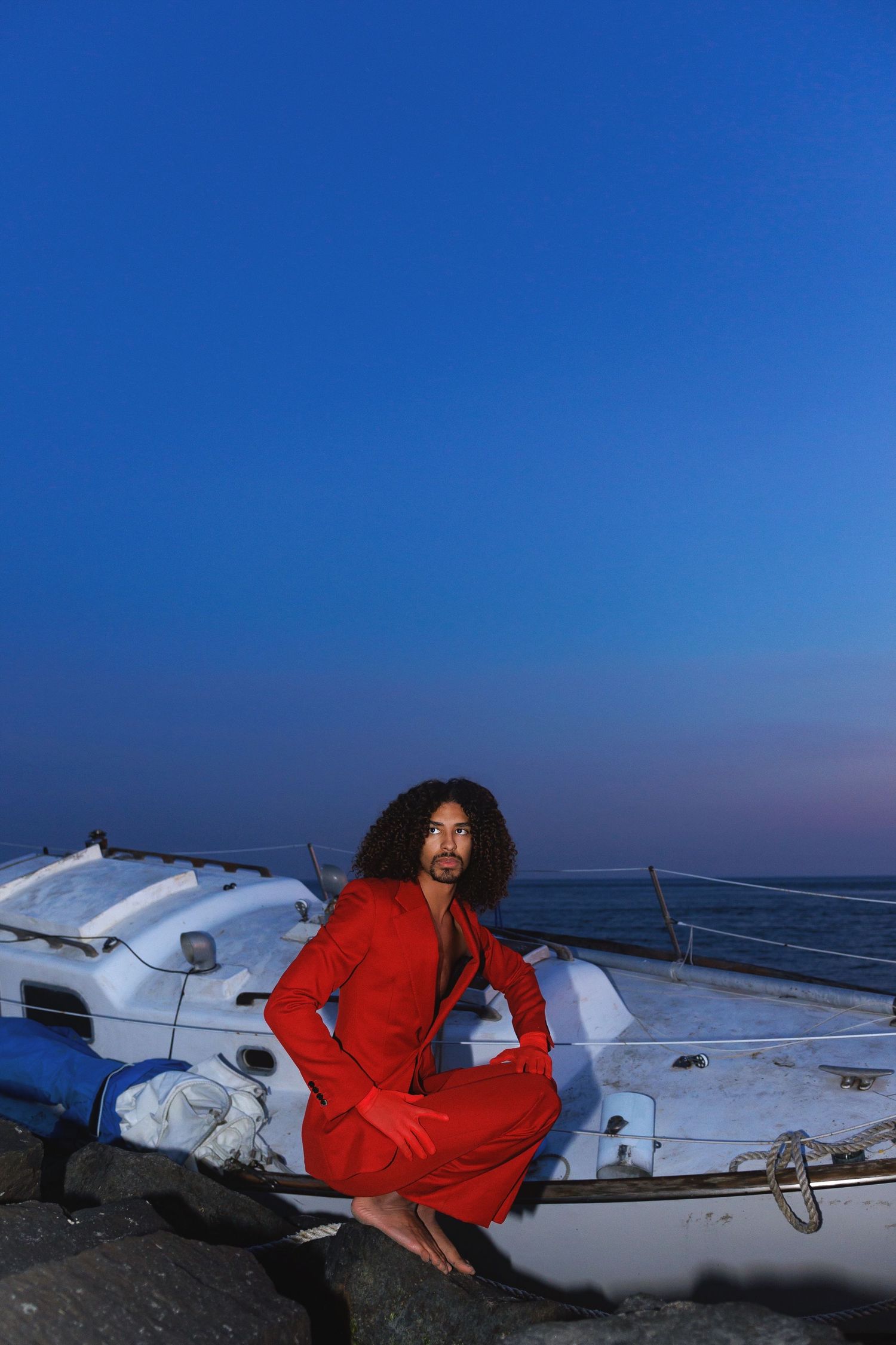 A person in a red jacket rests on the wing of a small aircraft against a deep blue sky background.