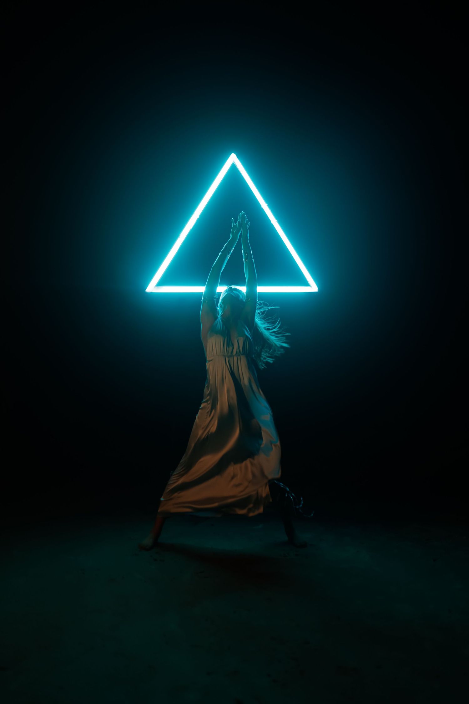 A silhouetted figure poses beneath a glowing neon triangle in a dark atmospheric setting.
