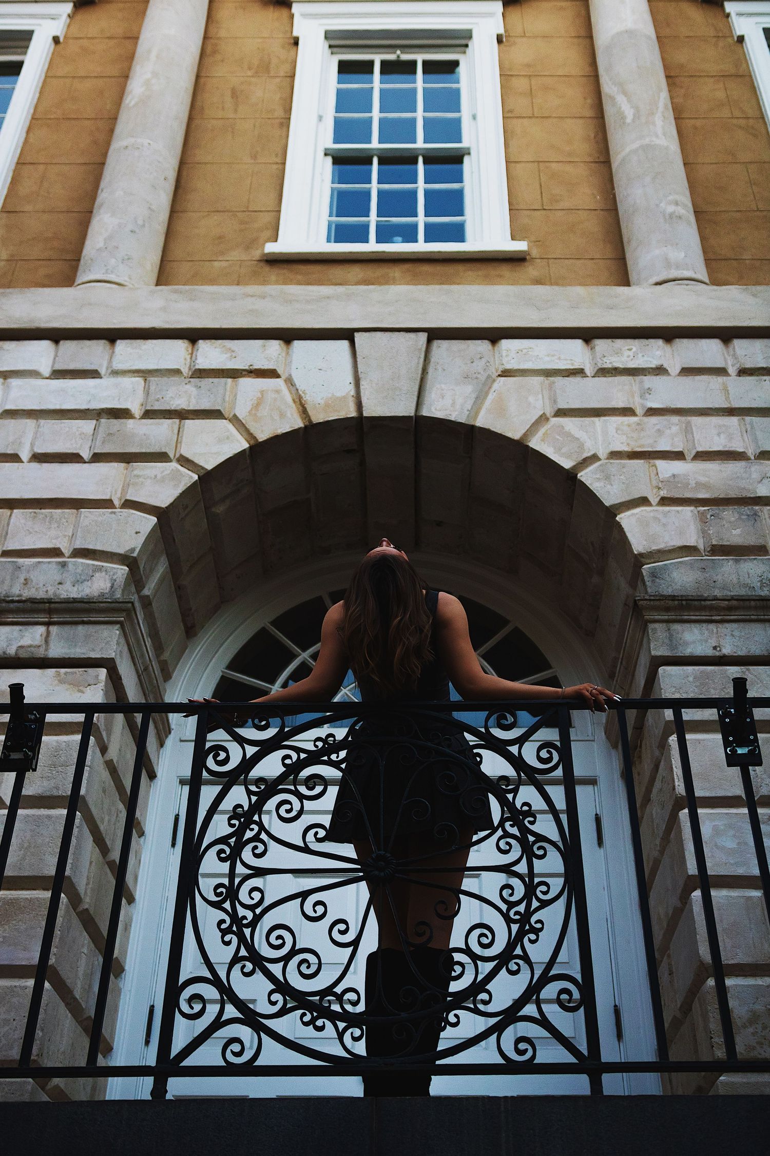 Silhouetted figure with umbrella stands beneath ornate stone archway of historic building with Georgian windows.