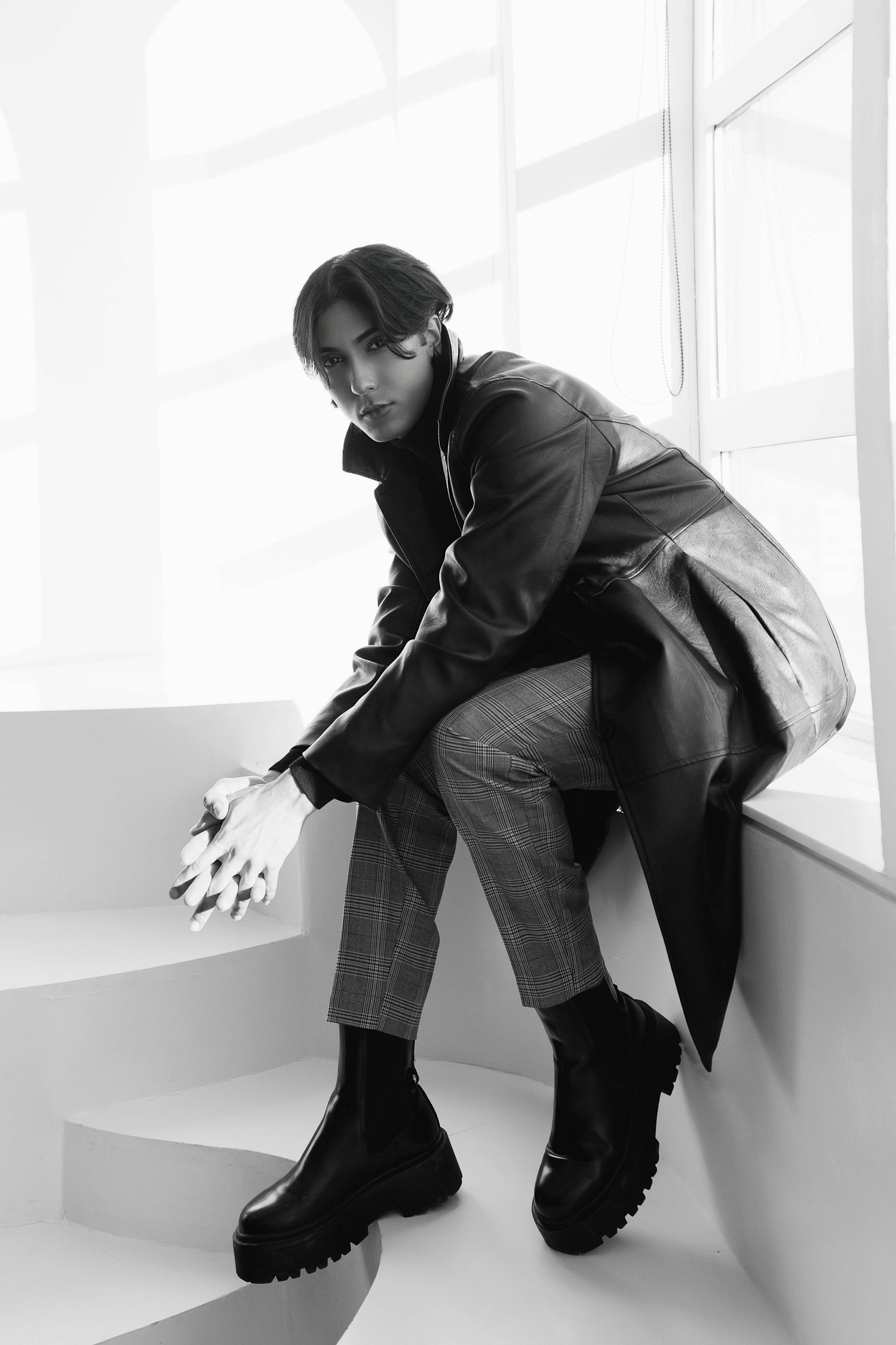 Black and white fashion photo of someone in chunky boots, plaid pants and dark coat posing on white steps.