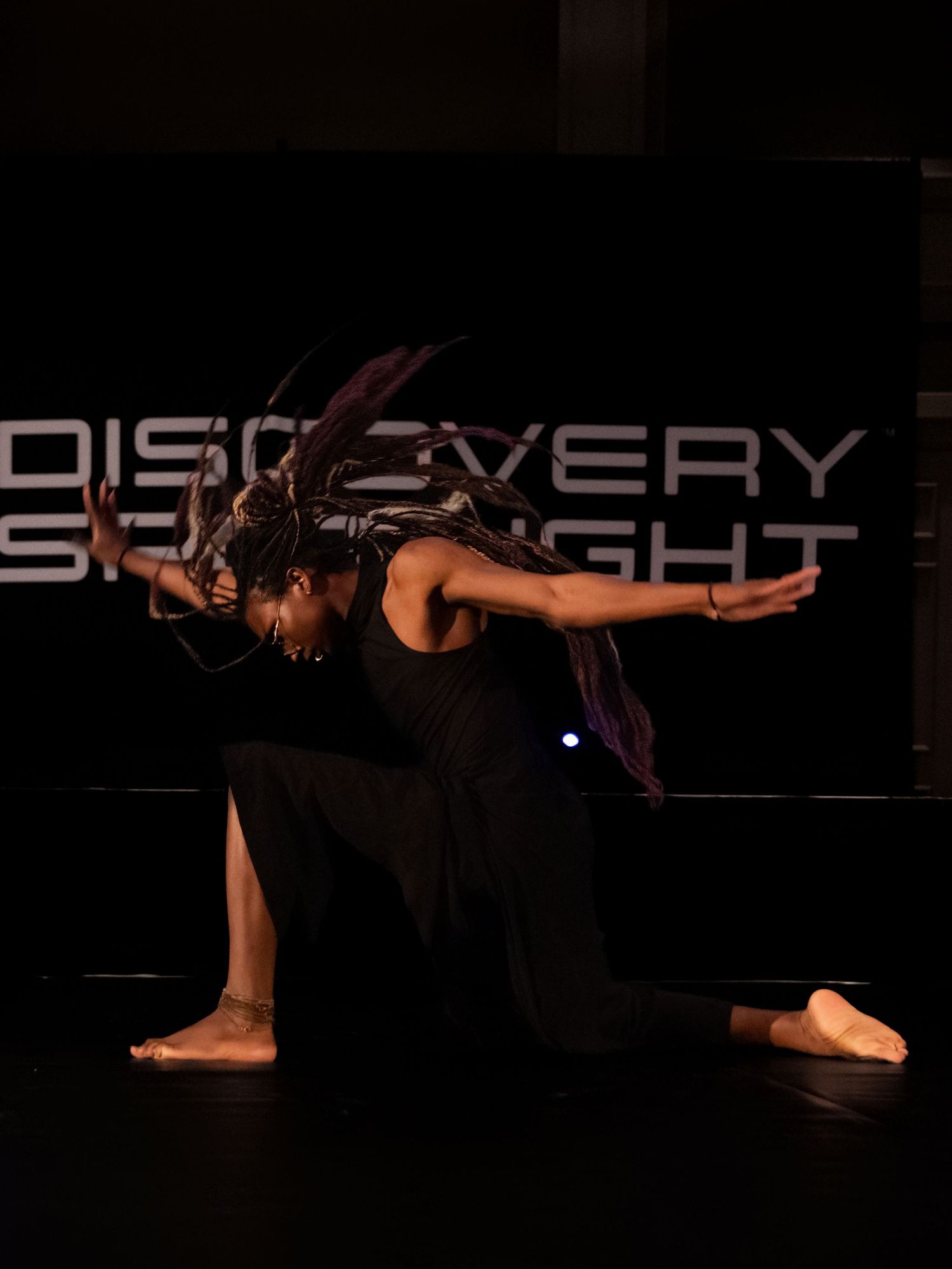 Dancers perform a contemporary dance piece in dramatic lighting on a dark stage.