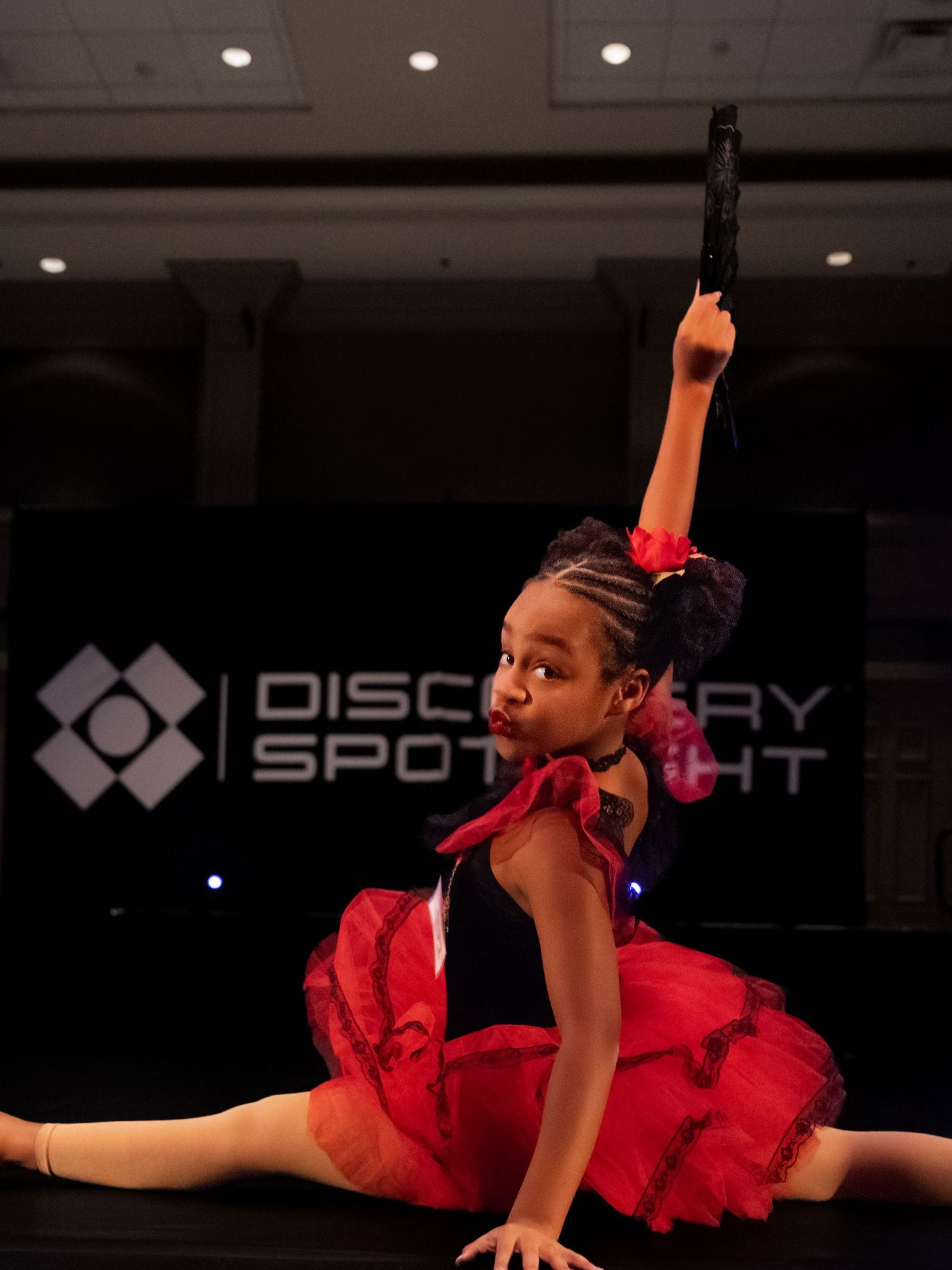 A dancer in a red tutu dress performs a graceful split leap during a dance performance on stage.