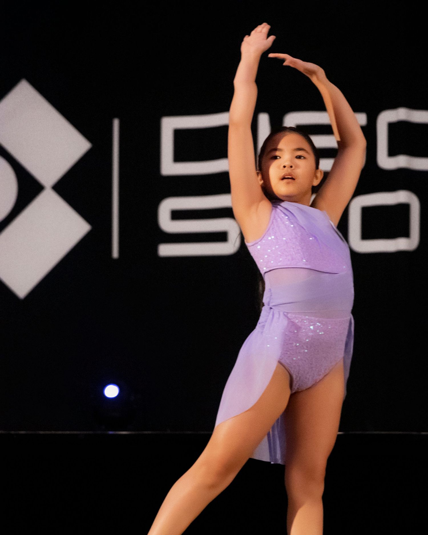 A figure skater in a lavender costume performs a graceful pose during an ice skating routine.