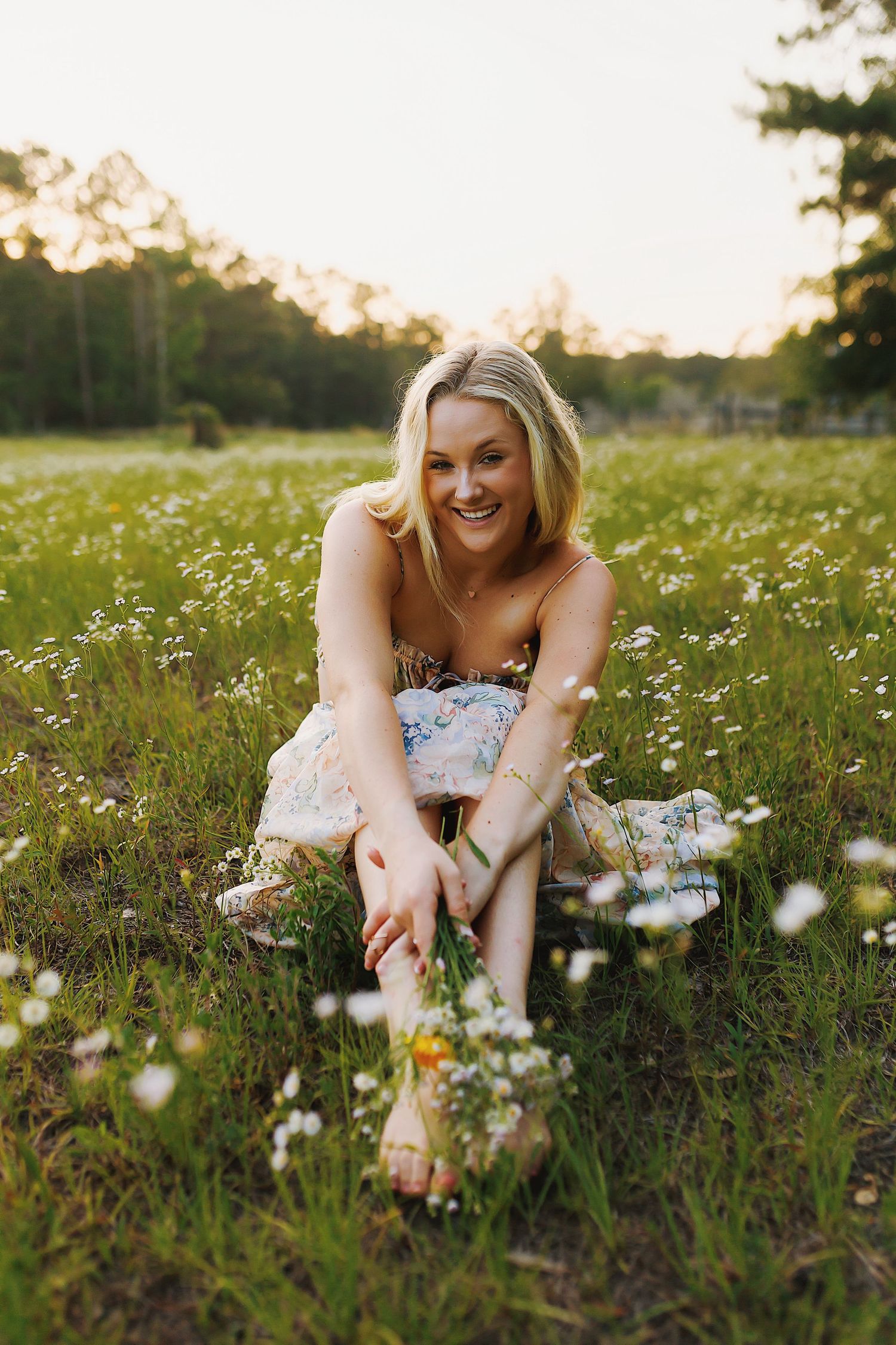 Graduate in white dress lying in a wildflower meadow during sunset.