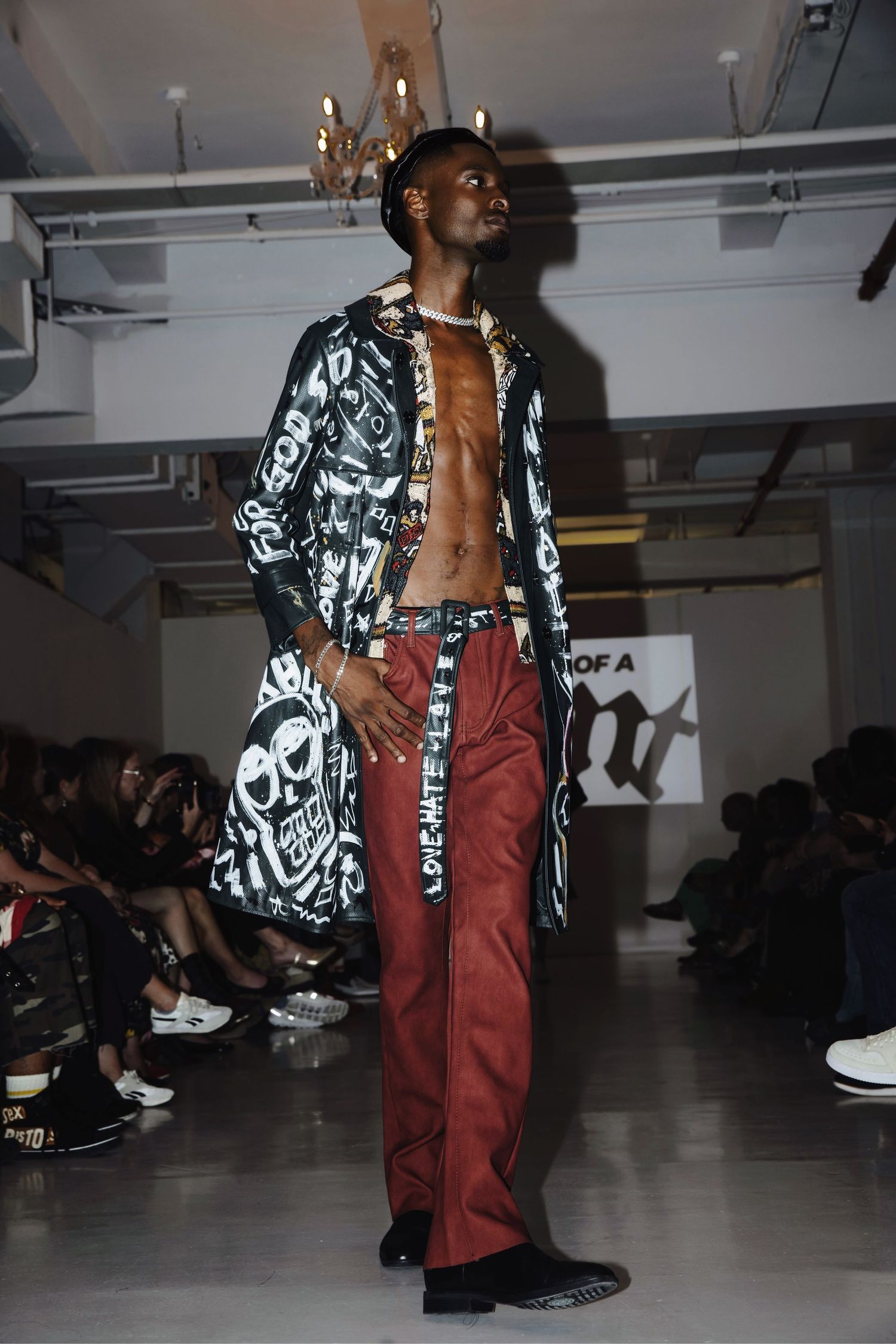 A fashion model walks the runway wearing black and white patterned jacket with burgundy pants during a fashion show.
