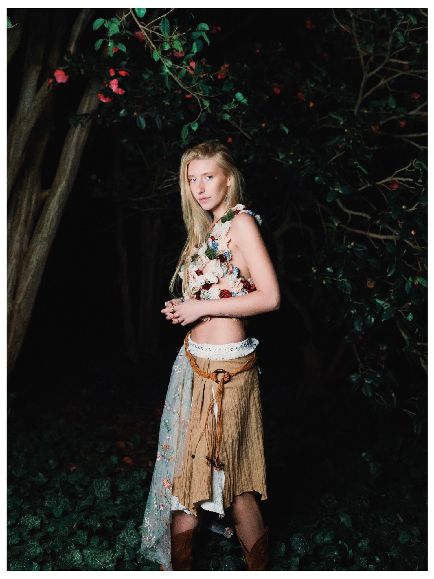 Fantasy themed photoshoot in dark forest setting with medieval-inspired costume and natural foliage backdrop at night.