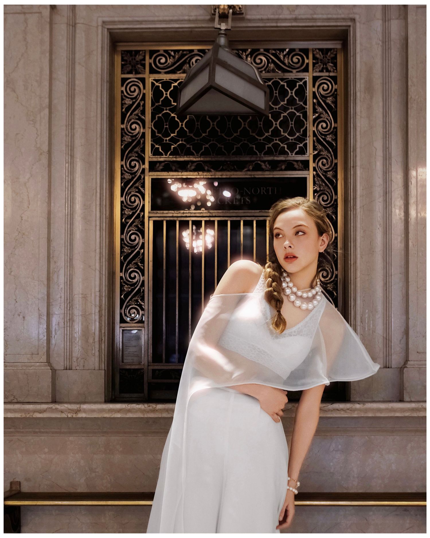 A model poses dramatically in a white avant-garde dress against ornate architectural elements in a vintage-style fashion shoot.