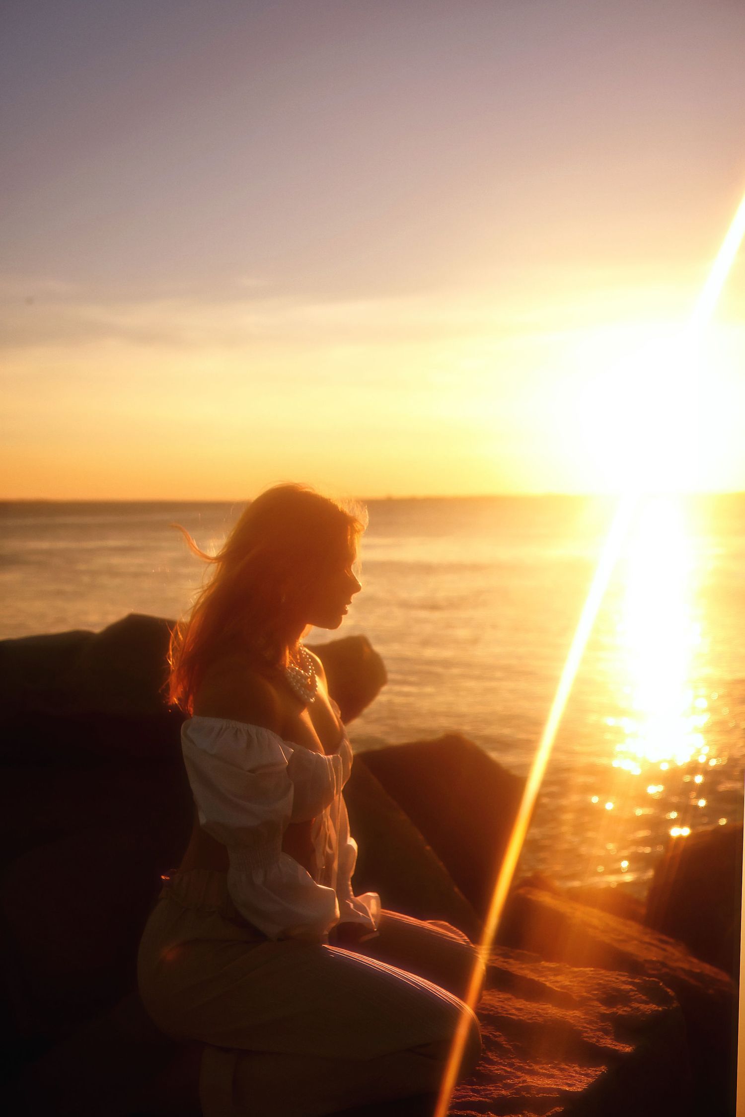 Silhouette of a person sitting on rocks by the ocean during a vibrant golden sunset.