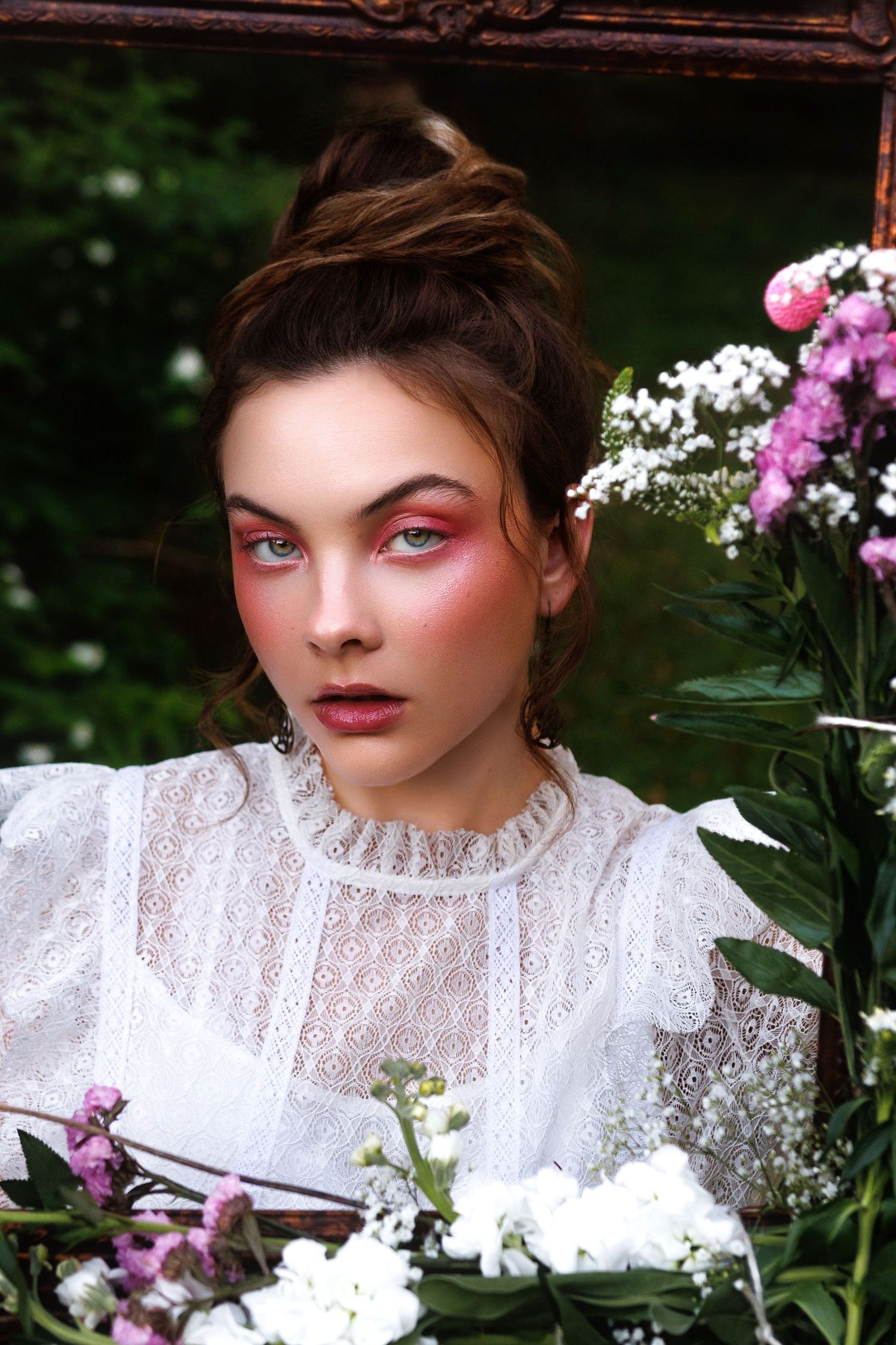 A romantic spring portrait featuring pink eye makeup, delicate white lace dress and blooming pink and white flowers in the frame.