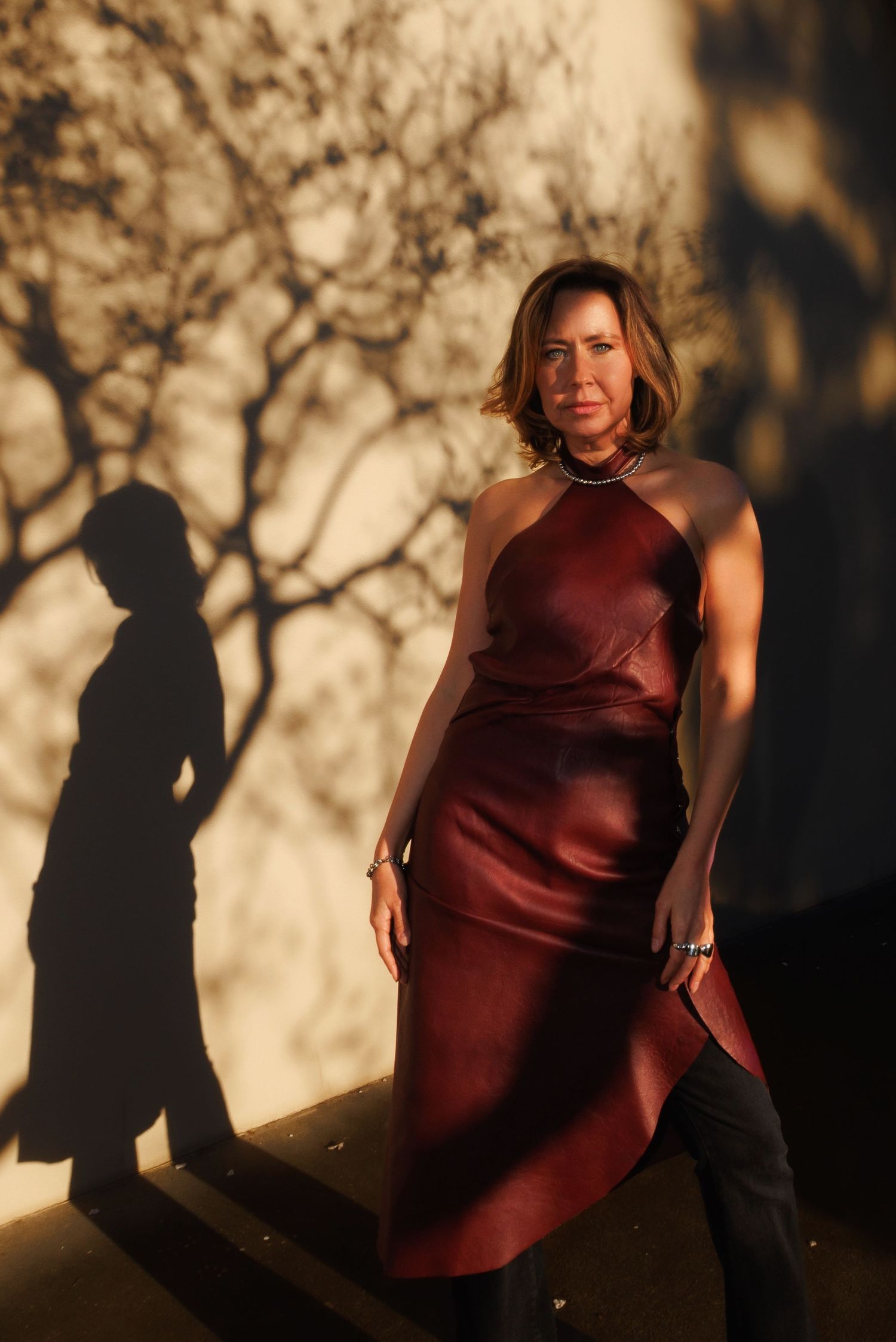 A sequence of silhouetted figures in burgundy dress cast dramatic shadows against a golden sunset backdrop.