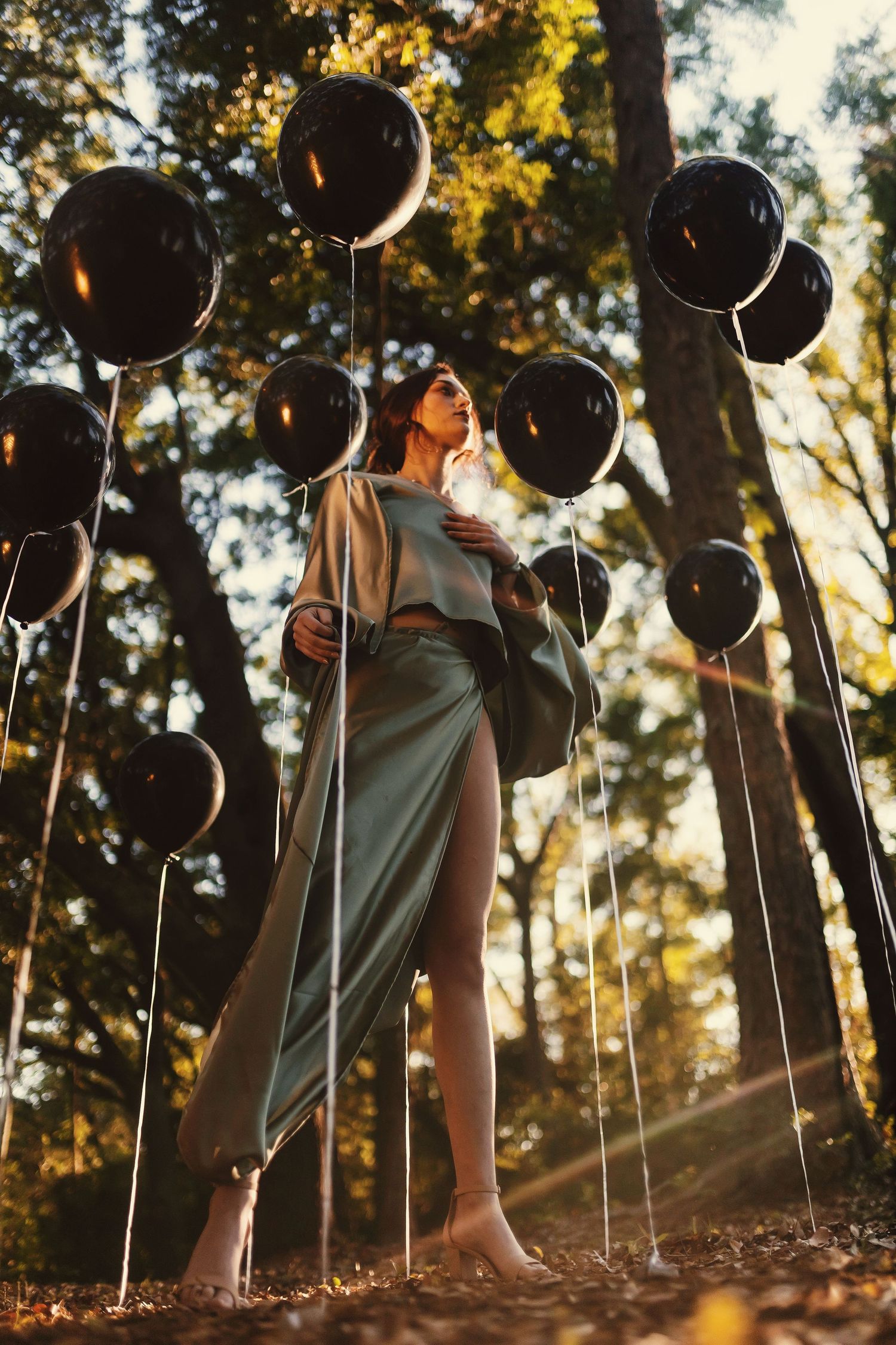 A row of black balloons held at ground level against a sunlit forest background with golden autumn foliage.