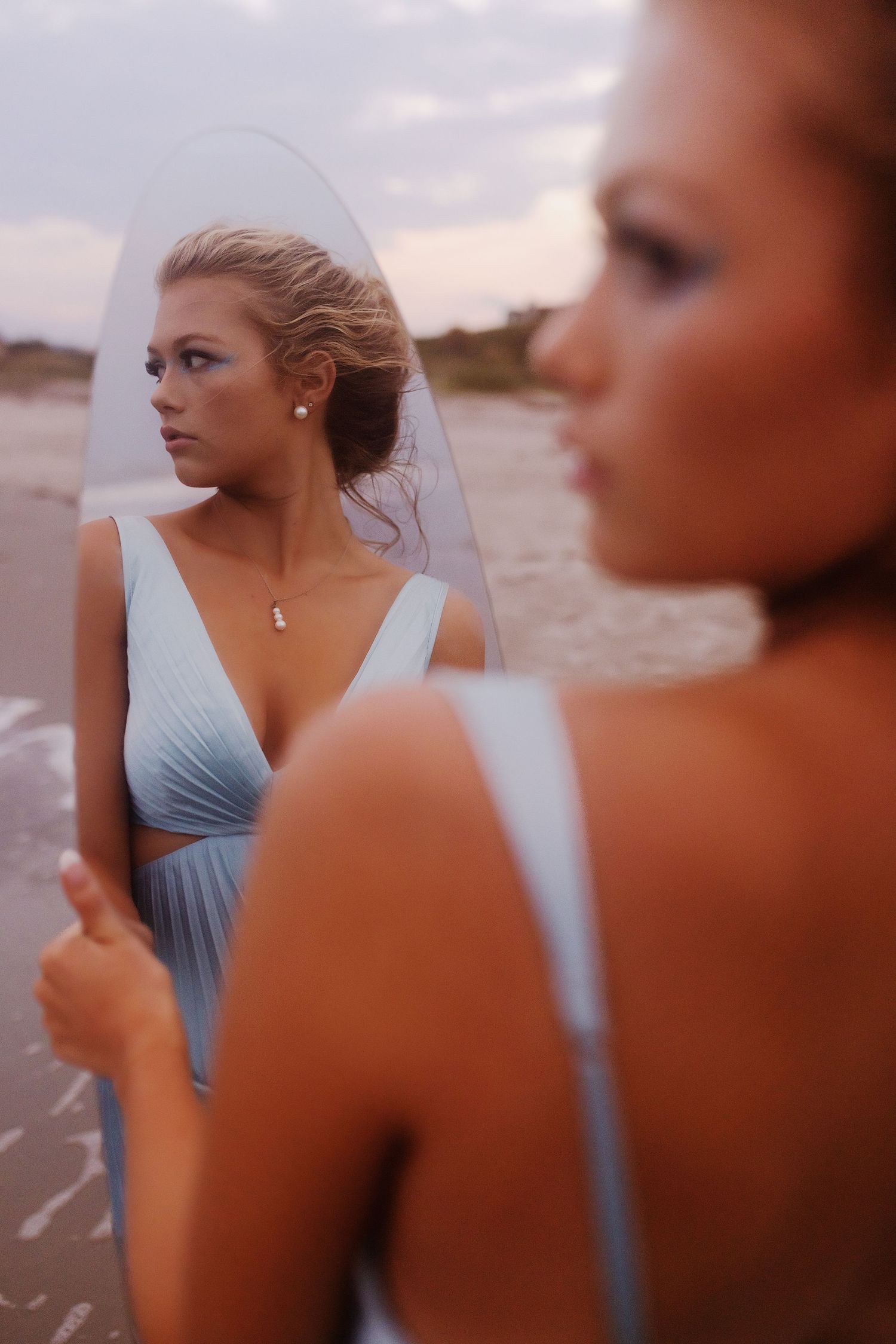 A group of women in matching blue dresses pose with surfboards on a sandy beach at dusk.