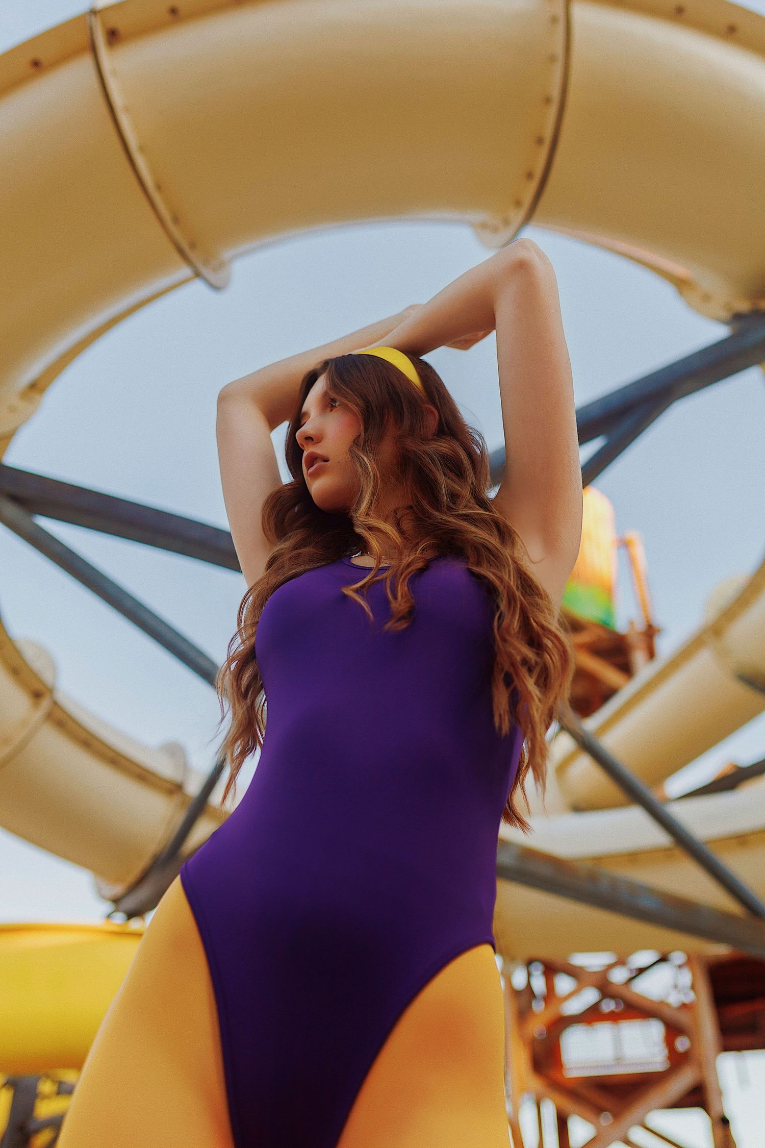 Person in purple swimsuit poses against yellow and beige geometric playground structure background.