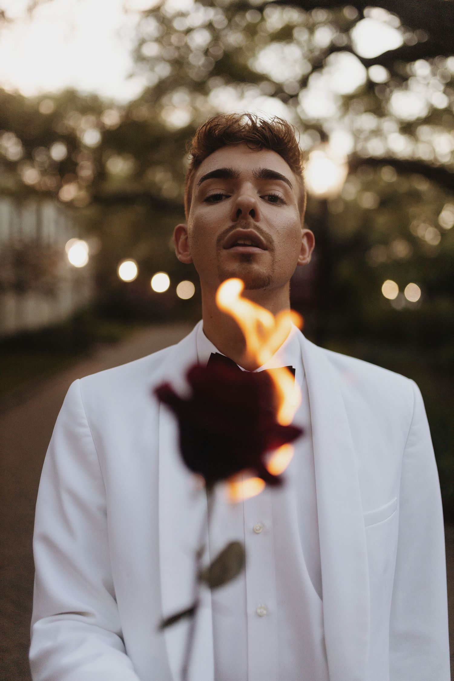 Artistic portrait of someone in a white suit jacket with a burning rose creating dramatic lighting at sunset.