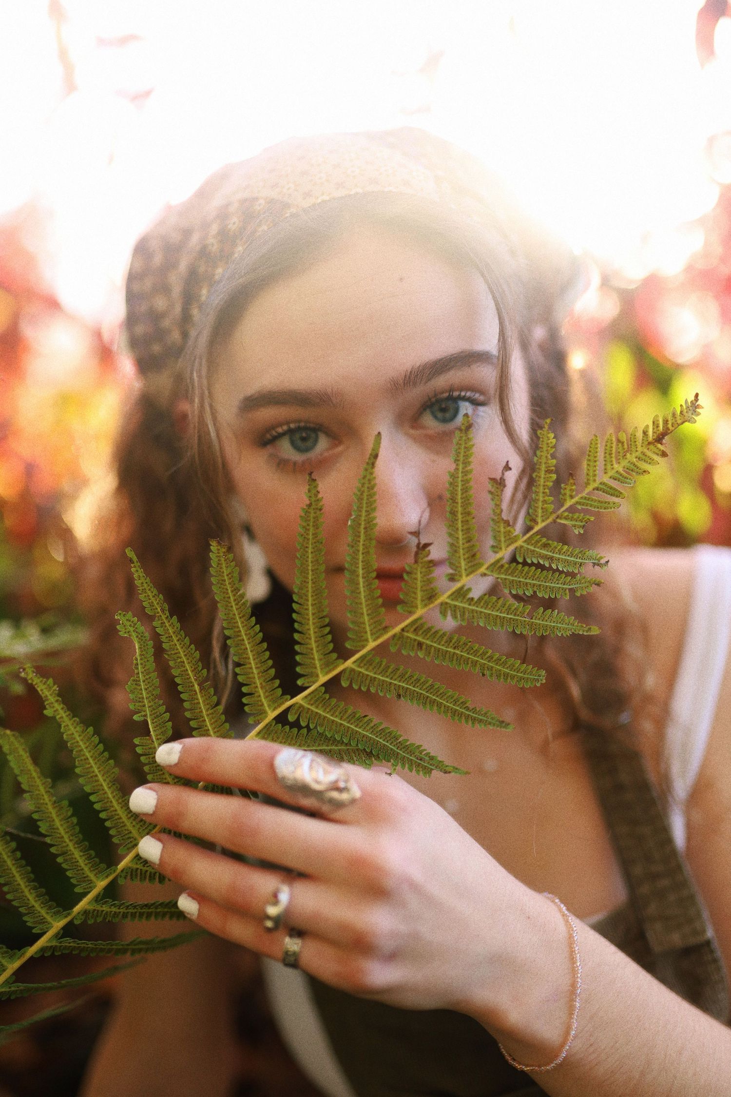 A dreamy portrait through fern leaves with soft natural lighting creates an ethereal mood.