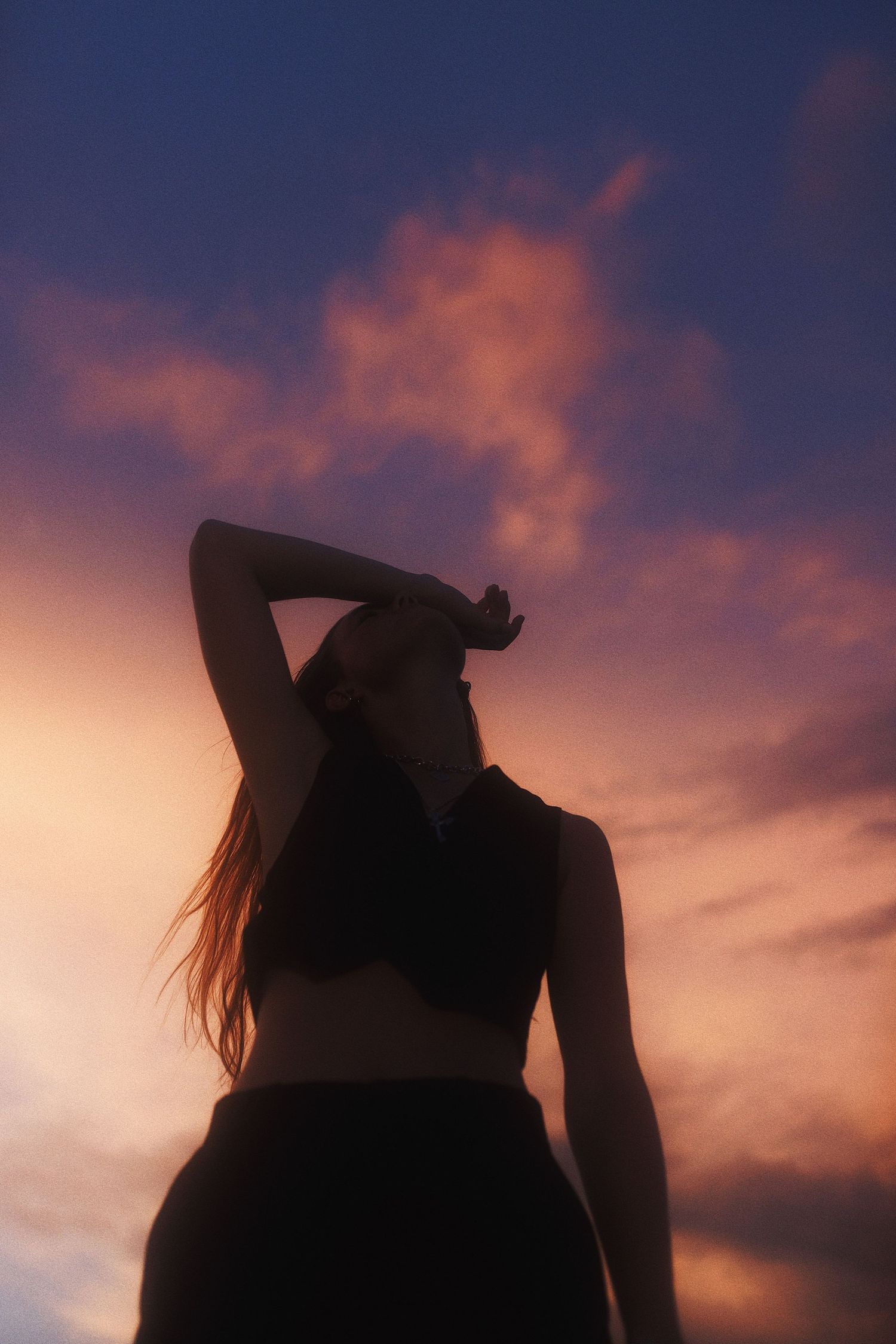 A silhouette of a figure with long hair against a dramatic purple and orange sunset sky.