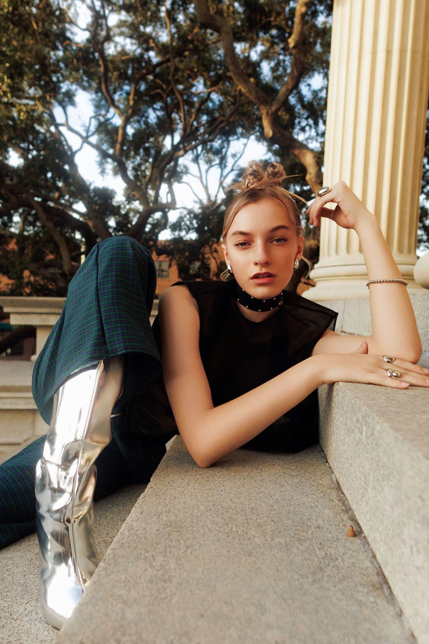 Fashion photography on concrete steps showing modern street style with metallic silver boots and black sleeveless top.