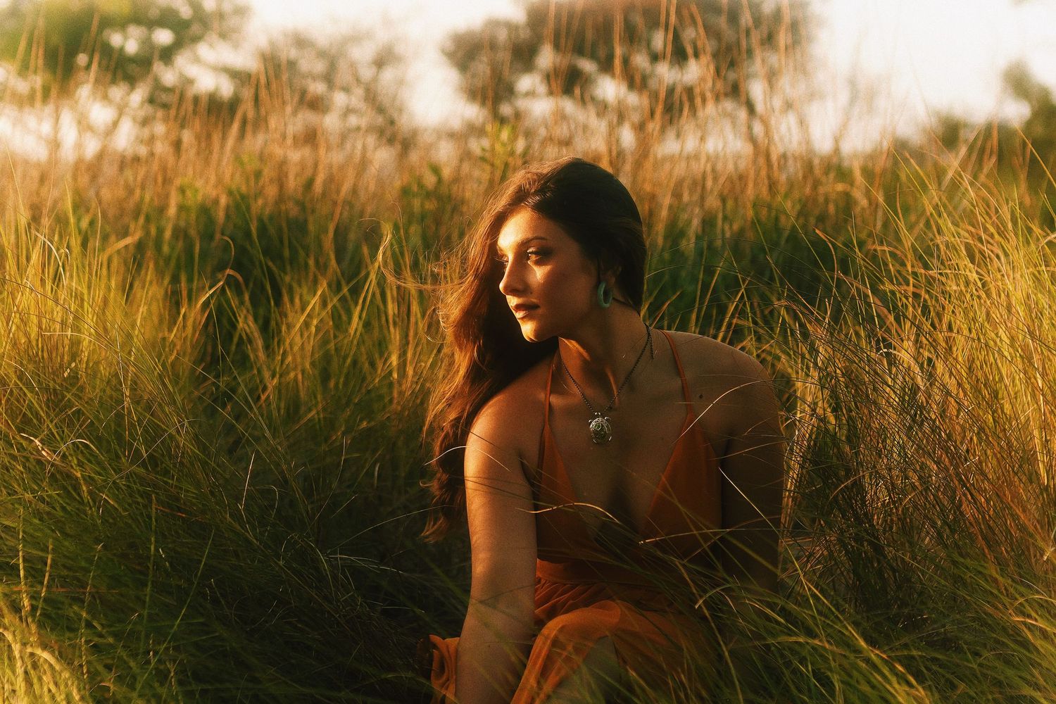 Silhouetted figures stand in tall golden grass during sunset creating a dreamy outdoor portrait session.