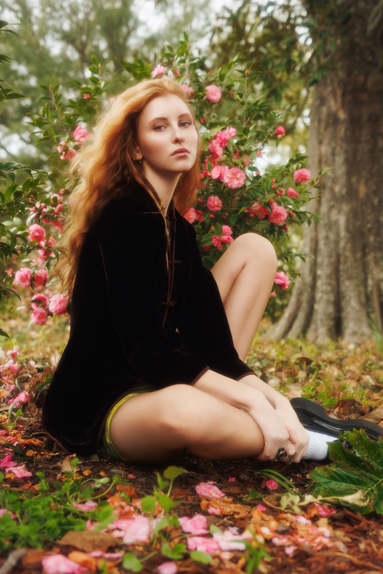 Person in black lounging among pink roses and fallen autumn leaves in a dreamy forest setting.