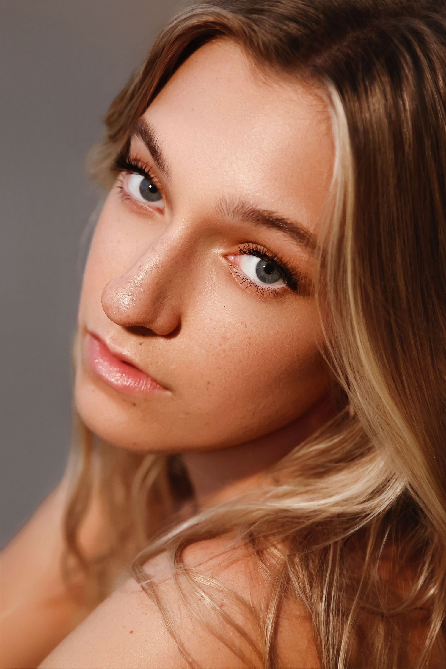 Closeup beauty portrait with natural makeup, blonde hair and soft lighting against neutral background.